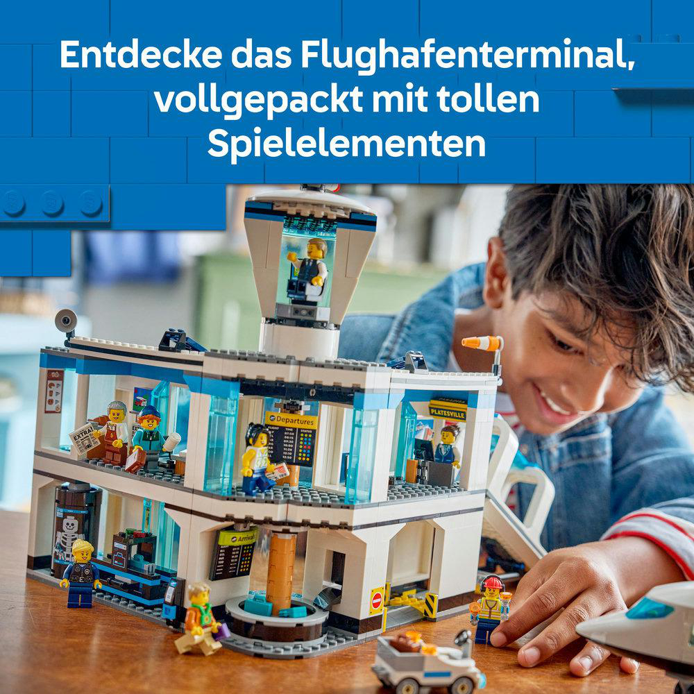 Ein Junge lächelt einen Lego-Flughafenterminal an. Das Terminal hat verschiedene Figuren und ein kleines Auto. Der Hintergrund hat ein blaues Muster.