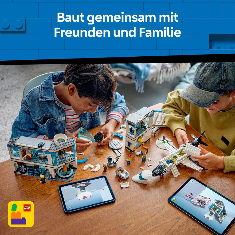 Zwei Kinder bauen Lego-Sets auf einem Holztisch. Die Sets umfassen ein Gebäude und ein Flugzeug. Zwei Tablets zeigen Bauanleitungen.