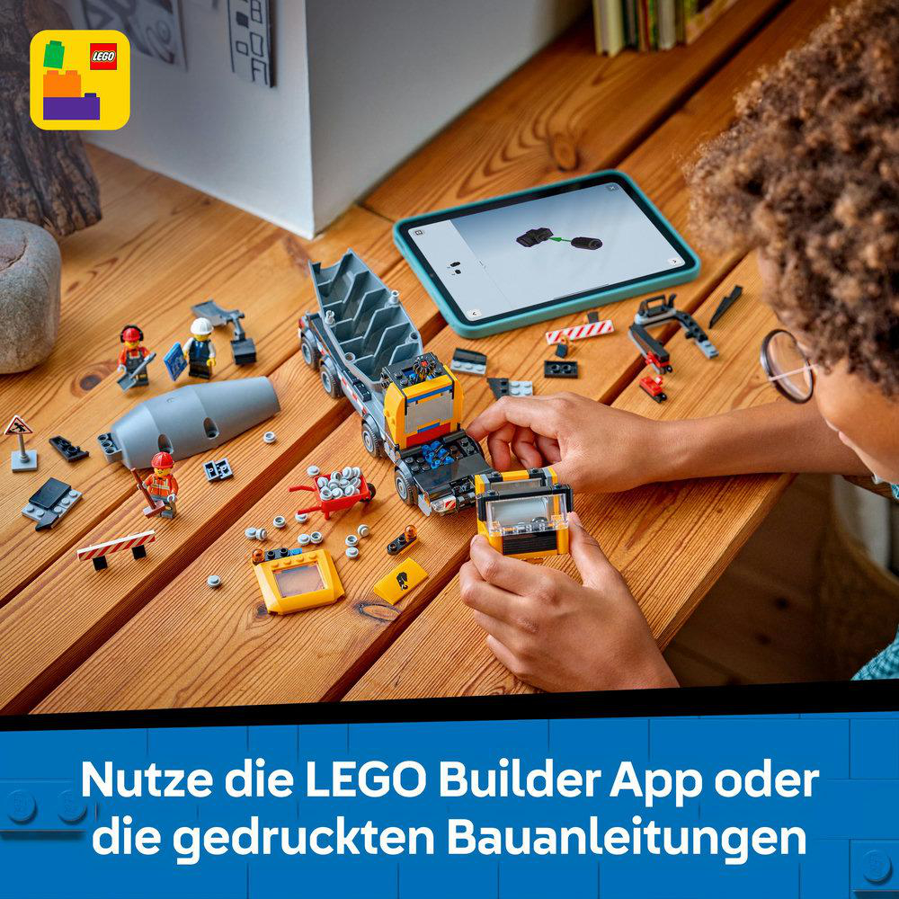 Eine Person baut einen Lego-Truck auf einem Holztisch. Es gibt ein Tablet mit Anweisungen. Viele Lego-Teile sind verstreut.