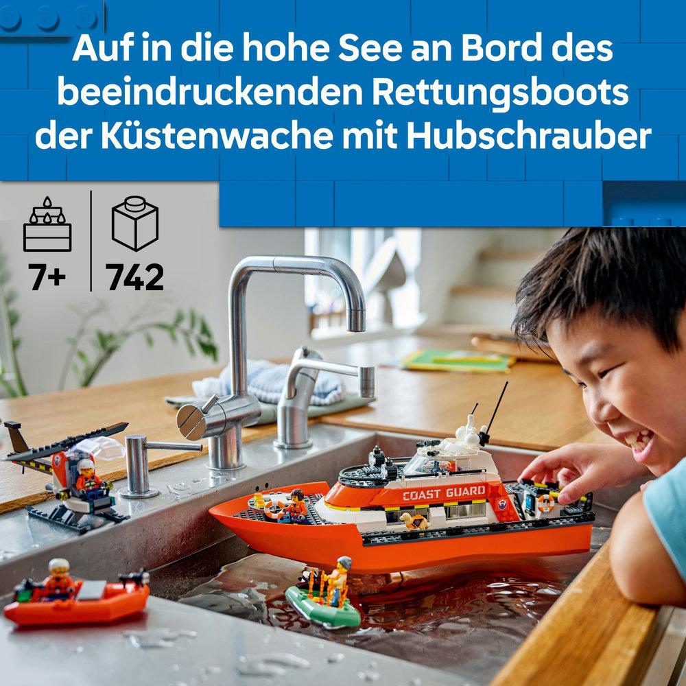 Ein Kind spielt mit einem Lego-Küstenwach-Rettungsboot in einem Waschbecken, mit einem Hubschrauber und einem kleineren Boot.