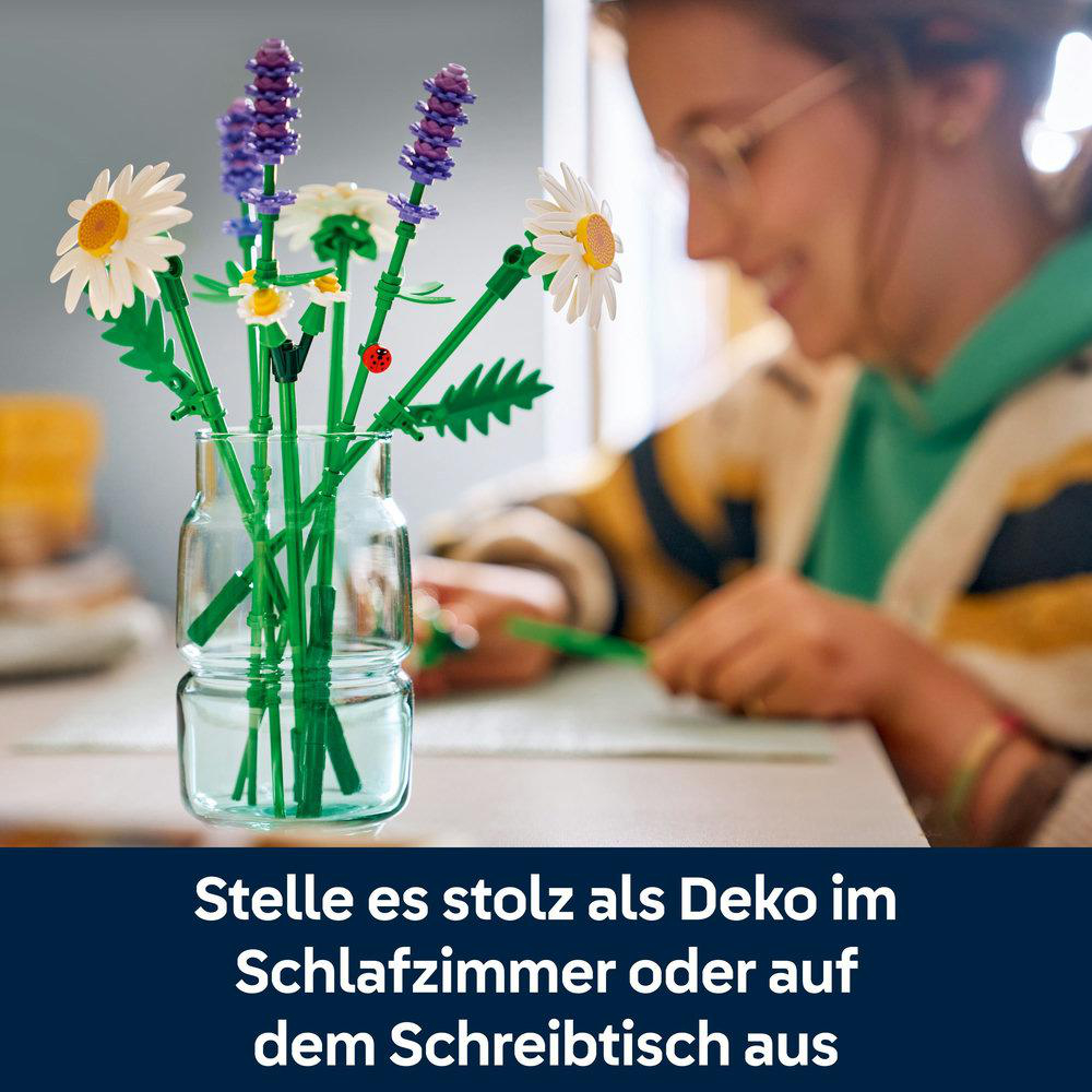 Eine Vase mit Lego-Blumen: Gänseblümchen, Lavendel und Grün. Im Hintergrund lächelt eine Frau.