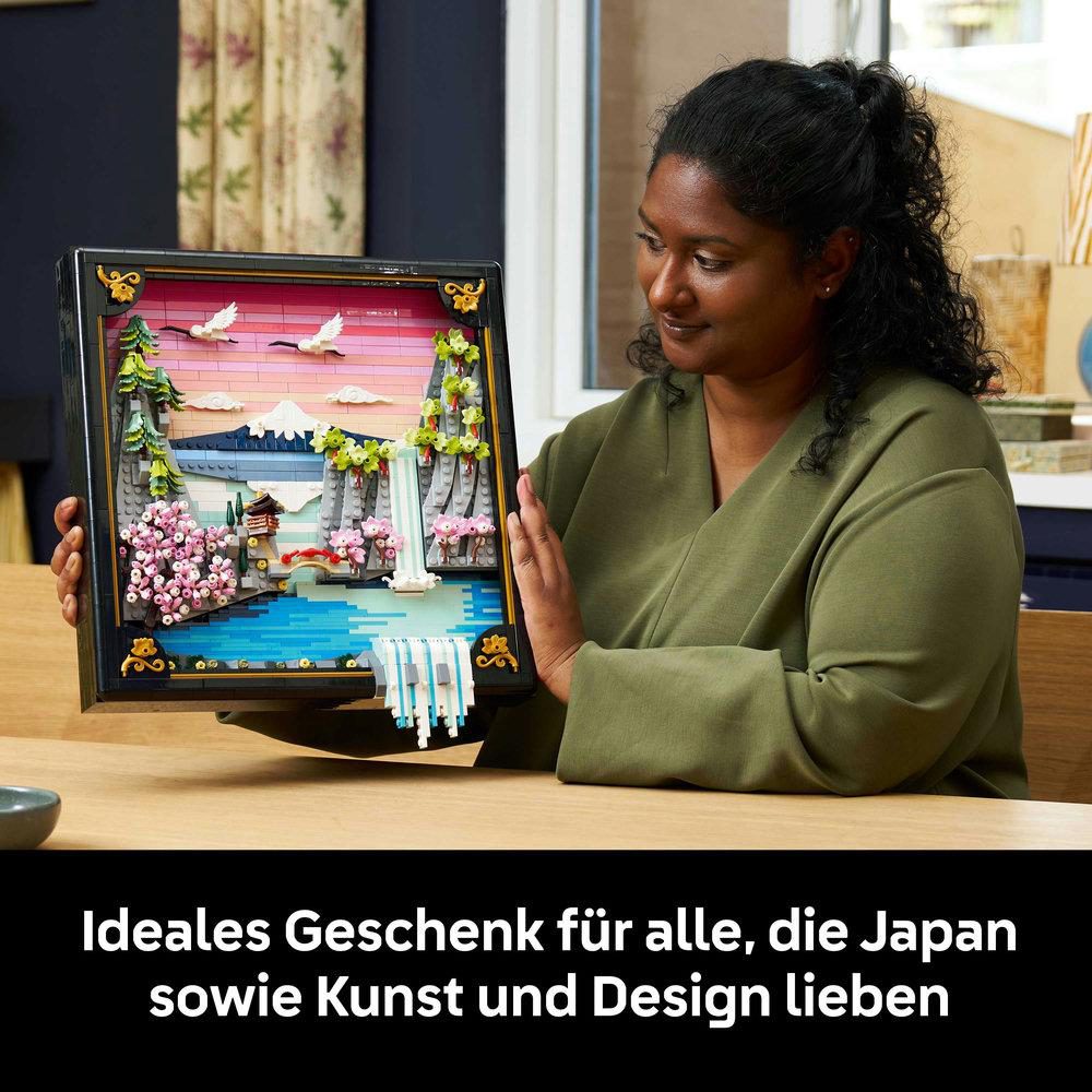 Eine Frau hält einen Lego-japanischen Garten. Der Garten zeigt einen Wasserfall, Kirschblüten und eine Brücke. Sie trägt ein grünes Hemd.