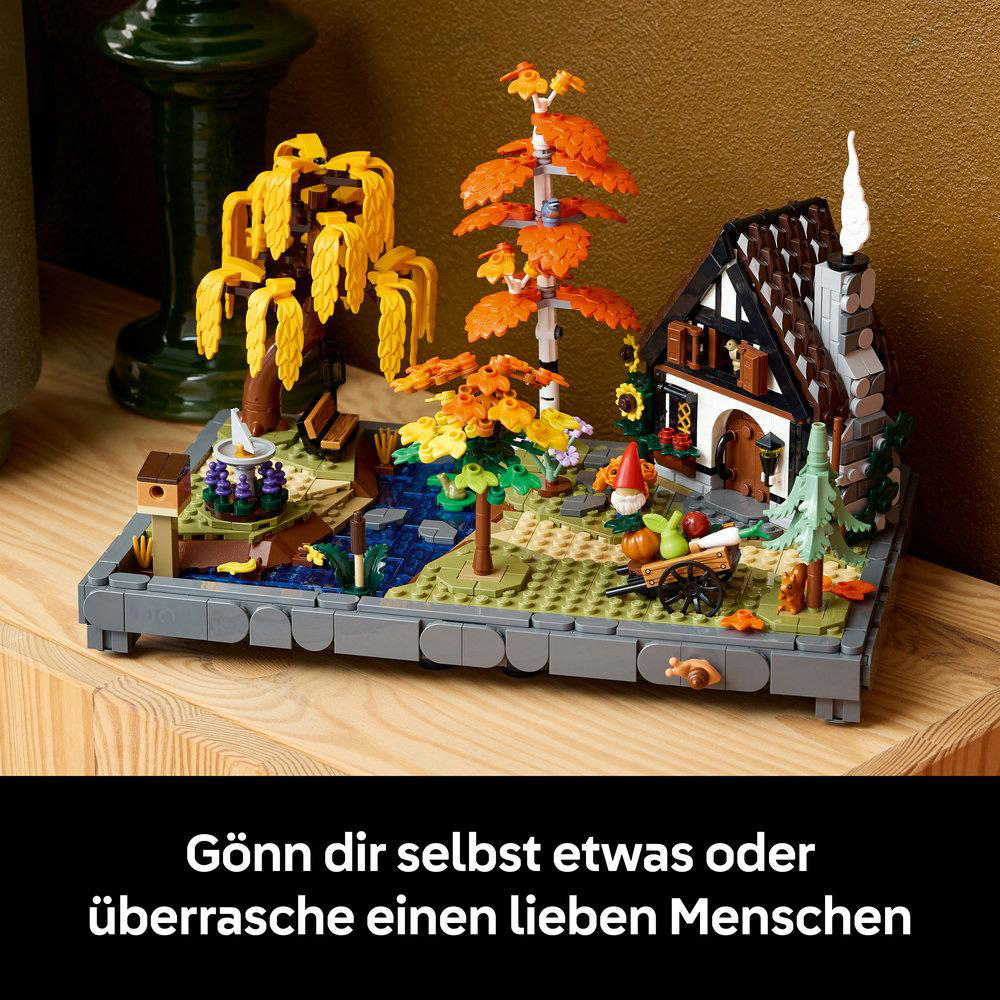 Ein Lego-Modell einer Dorfszene mit Haus, Bäumen, Bach und Zwerg. Die Szene befindet sich auf einer Holzoberfläche.