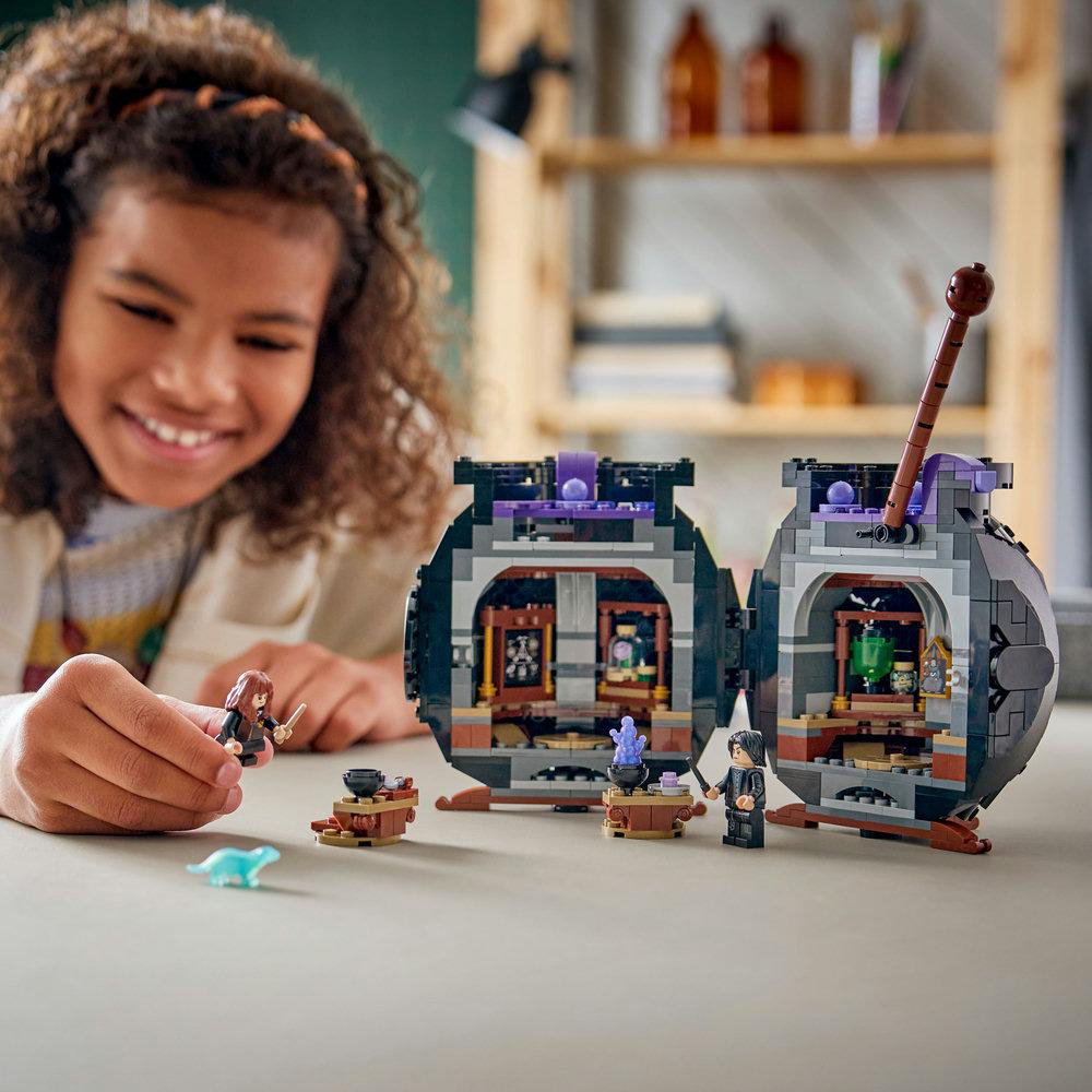 Ein Mädchen lächelt ein LEGO-Set an. Das Set zeigt zwei offene, kesselförmige Strukturen mit Mini-Figuren und Zubehör.