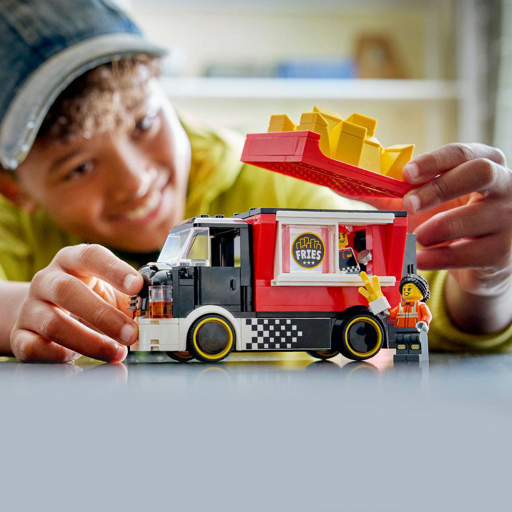 Ein Kind spielt mit einem Lego-Imbisswagen. Der Wagen ist rot und weiß mit einem Pommes-Logo. Das Kind hält Pommes.