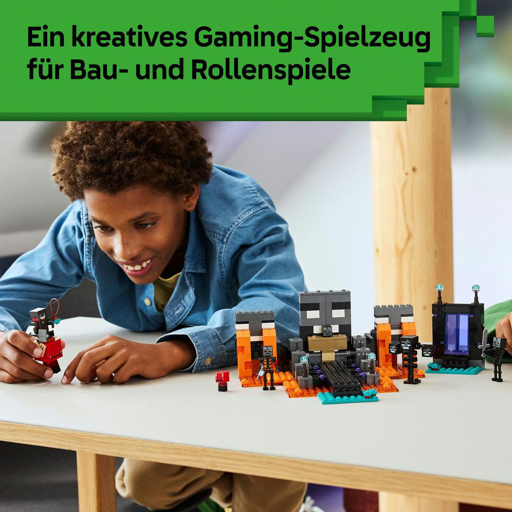 Ein lächelnder Junge spielt mit einem Minecraft-Lego-Set auf einem weißen Tisch. Das Set enthält Figuren und Strukturen mit orange und schwarz.