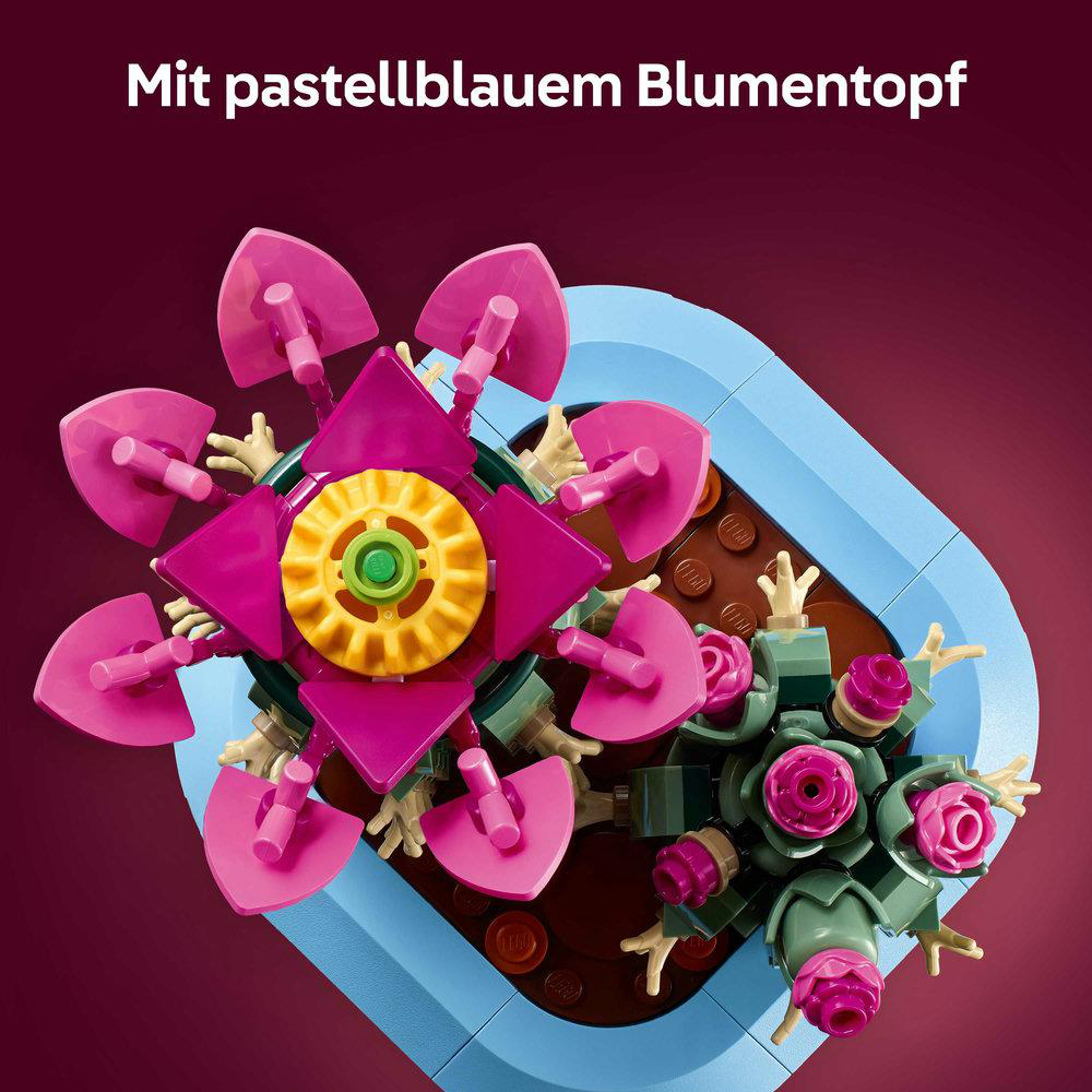 Ein Lego-Blumenarrangement in einem pastellblauen Topf. Die Blumen sind rosa und gelb mit grünen Akzenten. Der Hintergrund ist lila.