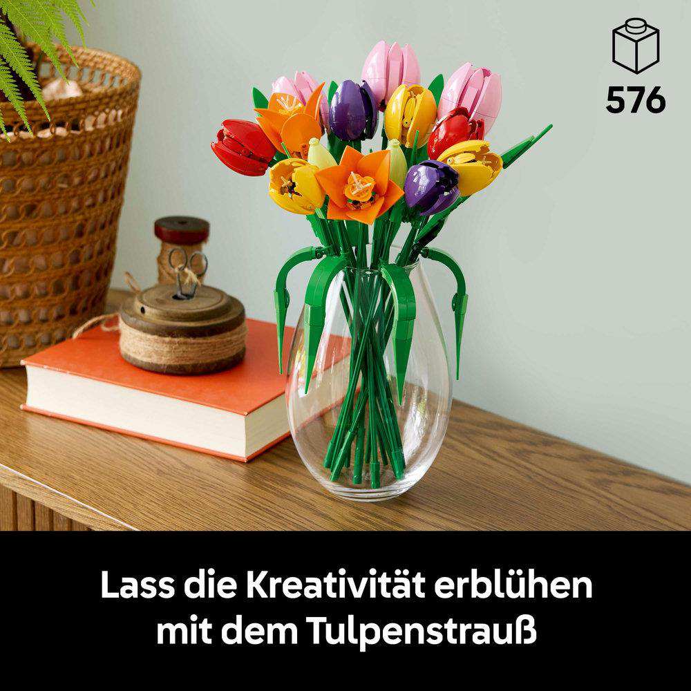 Ein Strauß bunter Tulpen in einer Glasvase. Auf einer Holzoberfläche befinden sich auch ein Buch und Dekorationsgegenstände.