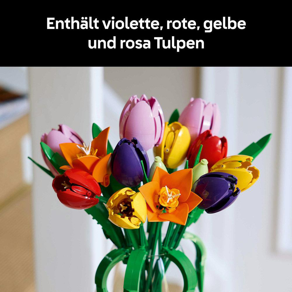 Ein Strauß bunter Tulpen, darunter lila, rote, gelbe und orangefarbene Blumen, in einer grünen Vase. Einige grüne Blätter sichtbar.