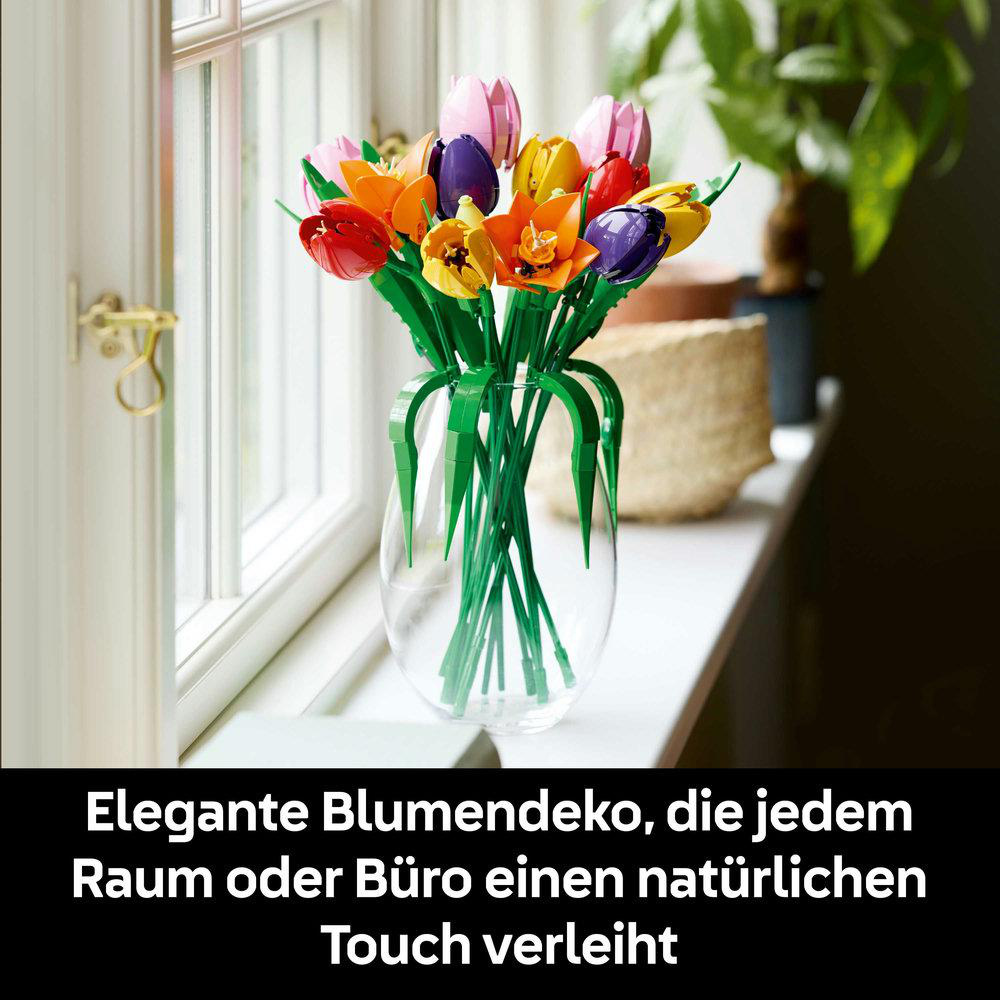 Eine klare Vase mit bunten Tulpen steht auf einer Fensterbank. Die Blumen sind rot, orange, gelb, rosa und lila.