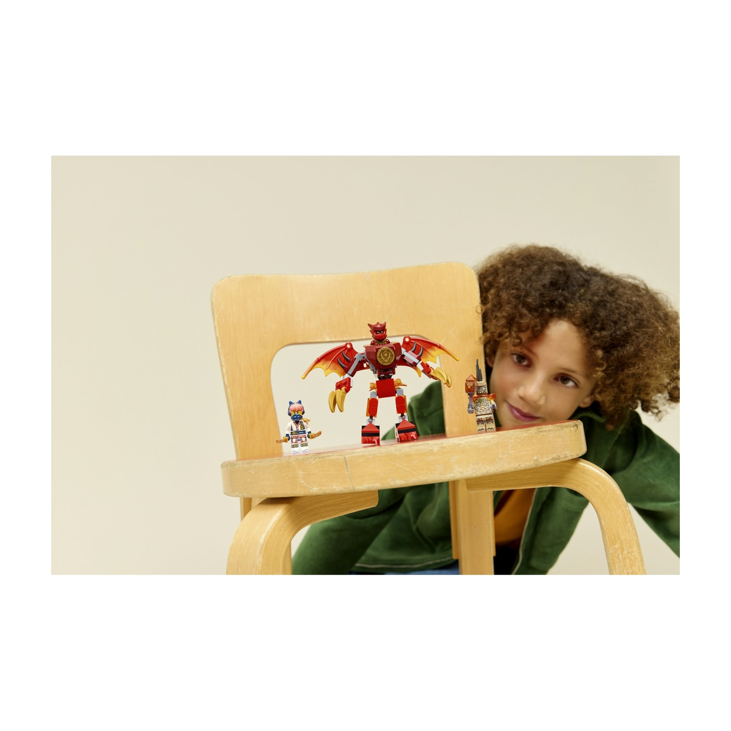 Un bambino guarda i personaggi Lego su una sedia di legno. Un robot drago rosso e altre due figure sono sulla sedia.