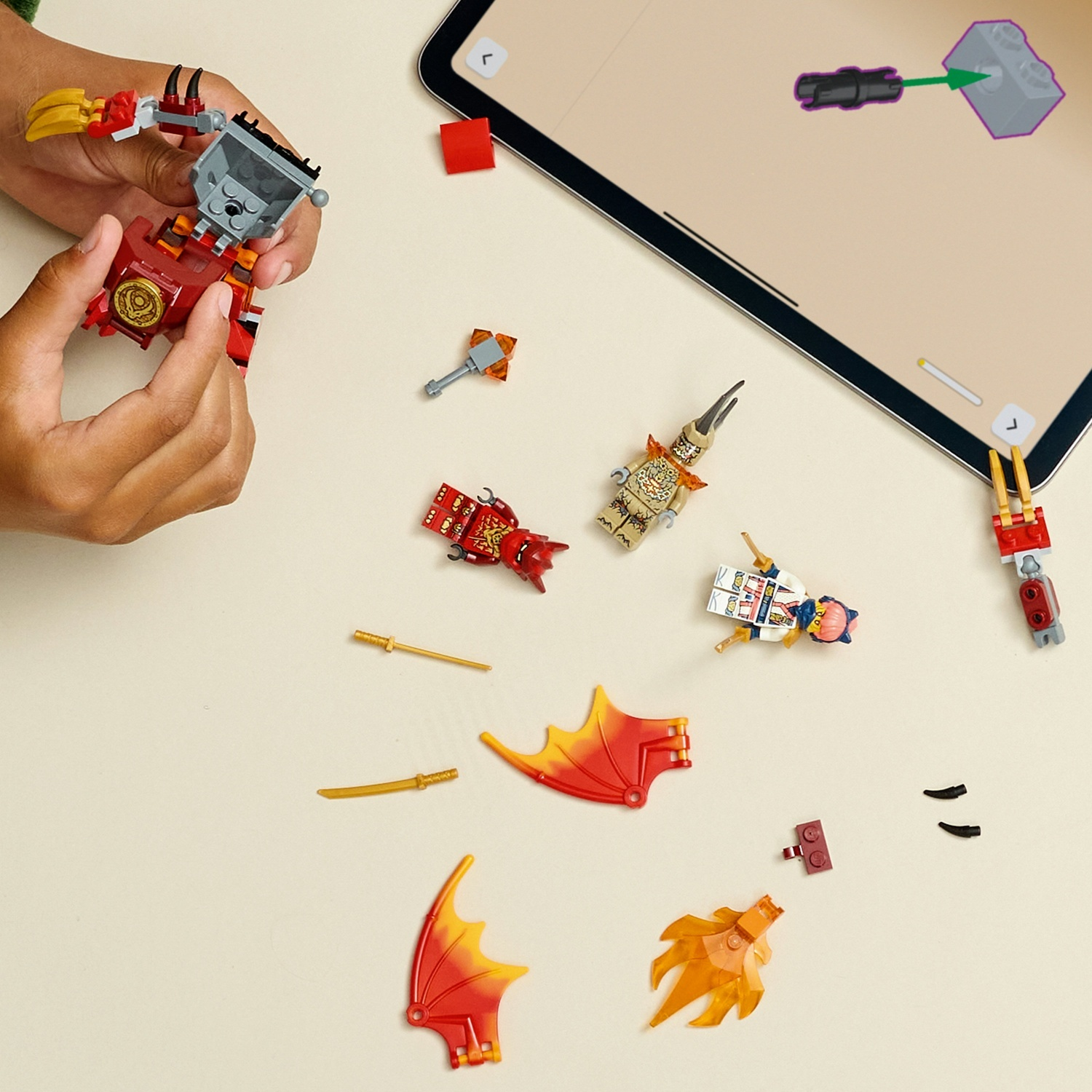 Mani che assemblano un robot Lego rosso e oro con altri pezzi Lego e istruzioni su un tablet, il tutto su una superficie beige.