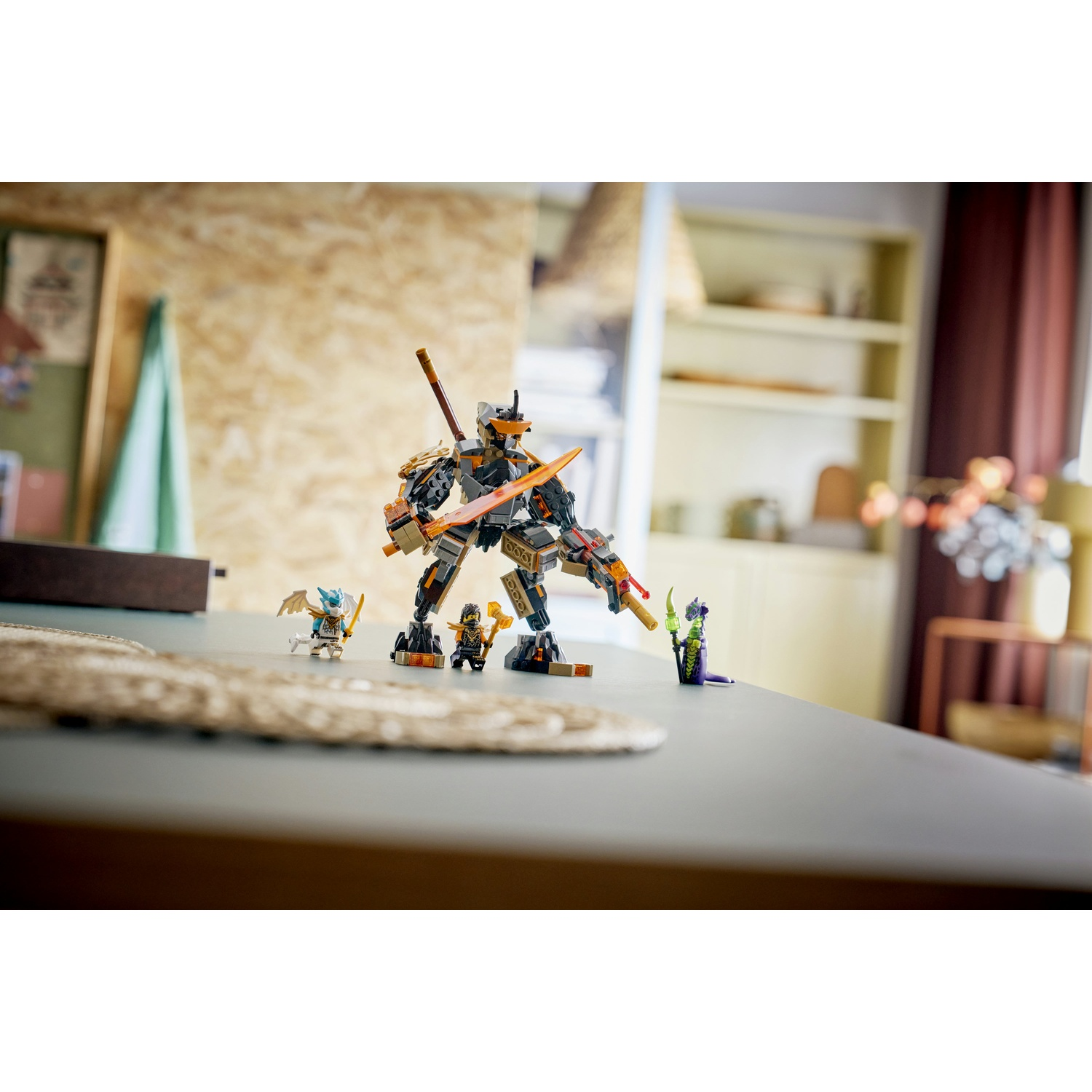 Un set LEGO Ninjago è esposto su un tavolo. Un grande mech è in piedi con personaggi più piccoli nelle vicinanze. Lo sfondo mostra una stanza con mobili.