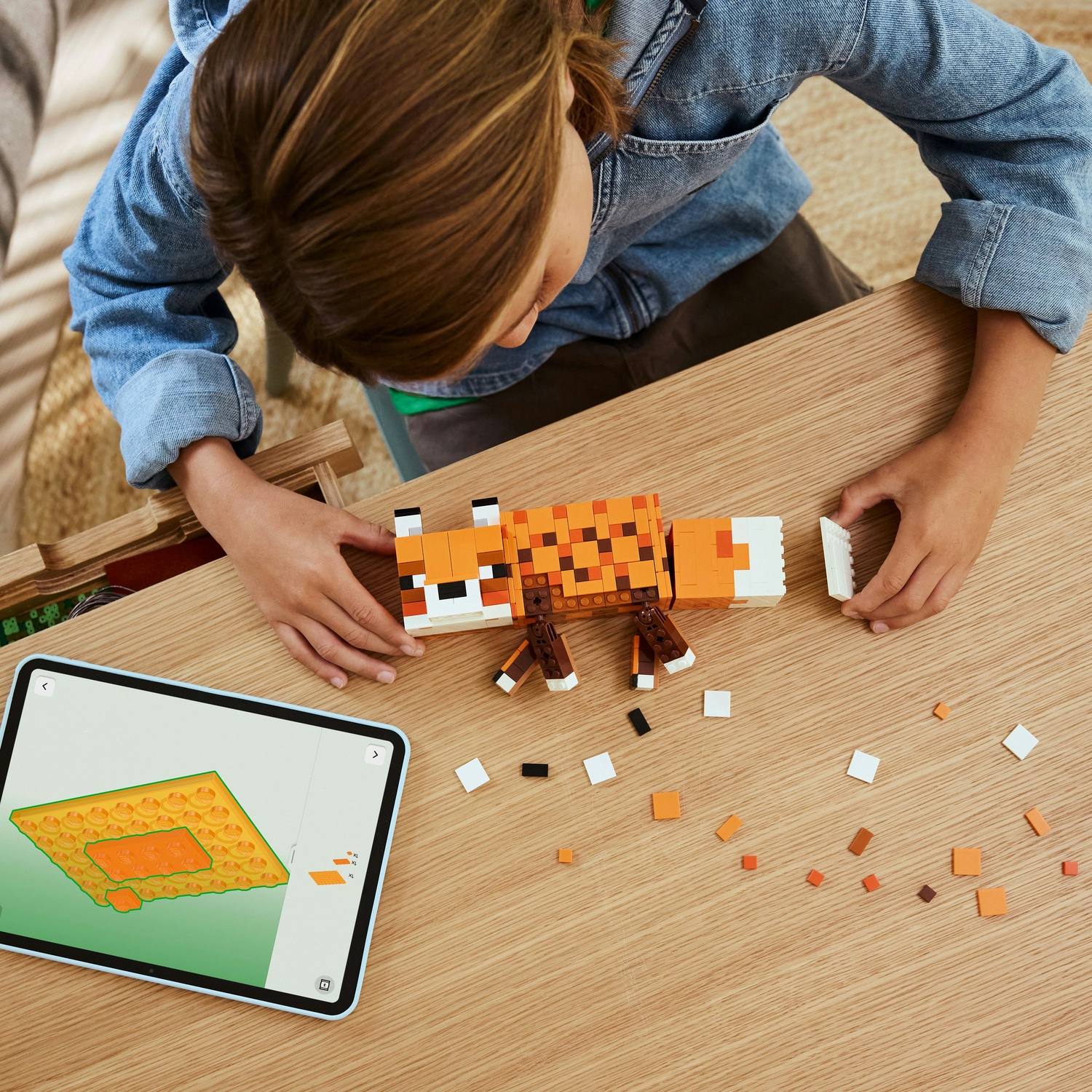 Un bambino assembla una volpe Lego su un tavolo di legno. Un tablet mostra le istruzioni. Pezzi Lego sparsi nelle vicinanze.