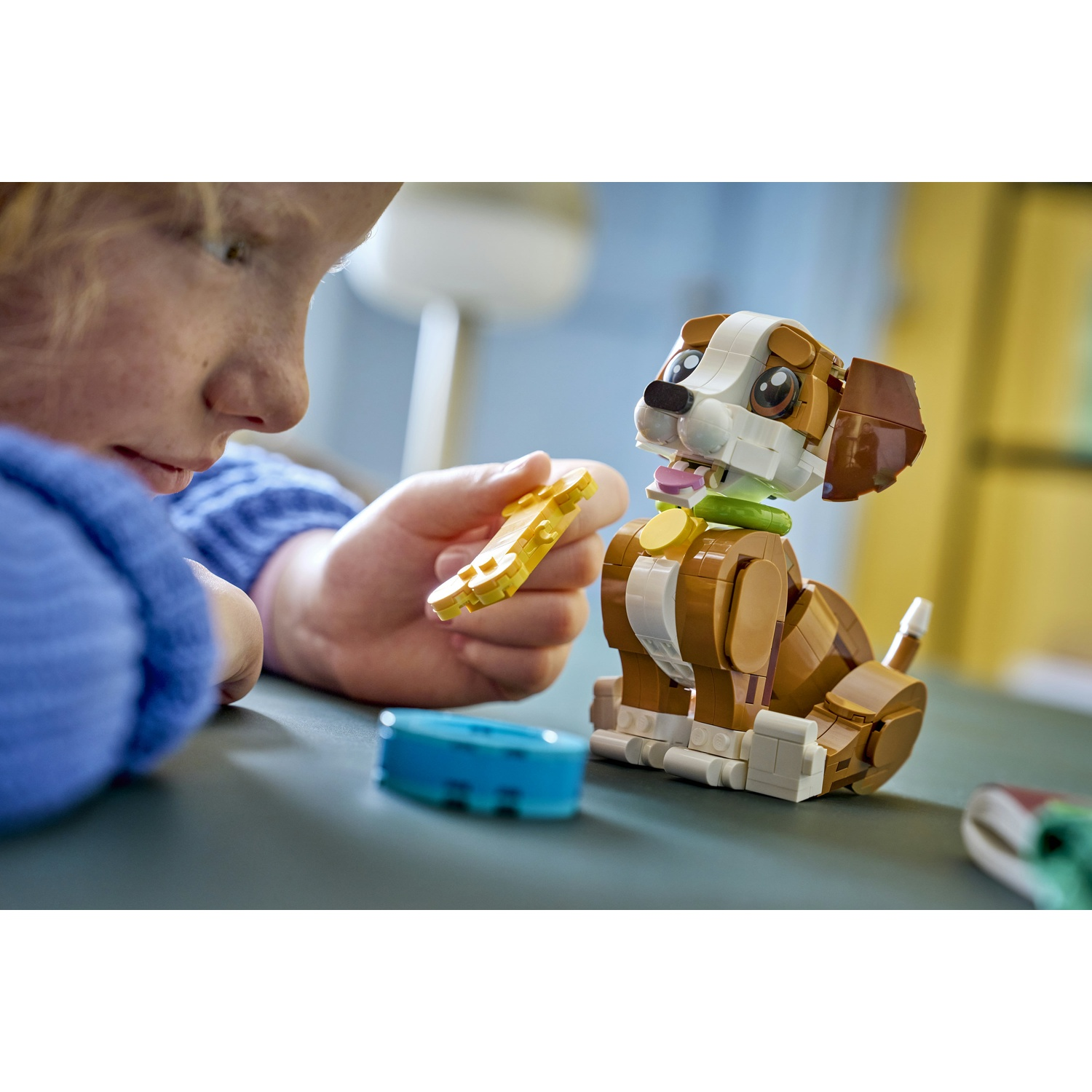 Una persona tiene in mano un pezzo Lego giallo, guardando un cane Lego. Una ciotola blu è sul tavolo.