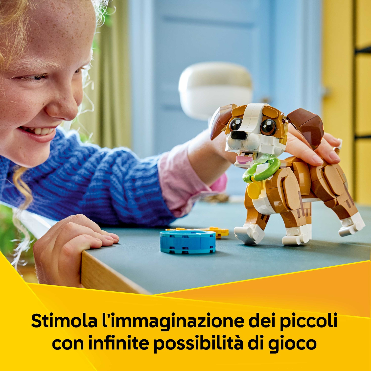 Una ragazza sorride, tenendo in mano un cane Lego. Il cane è marrone e bianco con un collare verde. Altri pezzi Lego sono su un tavolo blu.