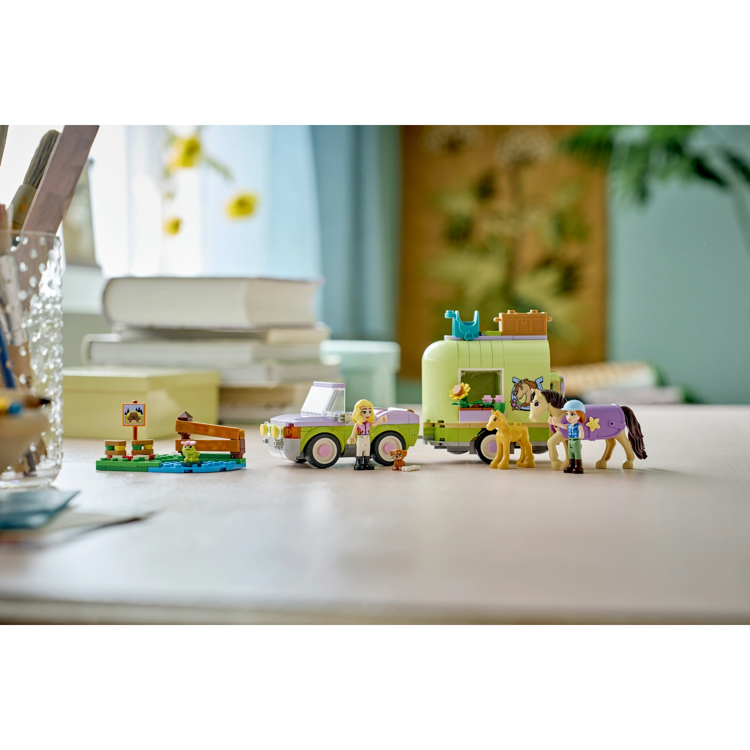 Set Lego con auto, rimorchio e cavalli. Sono presenti delle figure. La scena include un piccolo stagno e un cartello. Fiori sullo sfondo.
