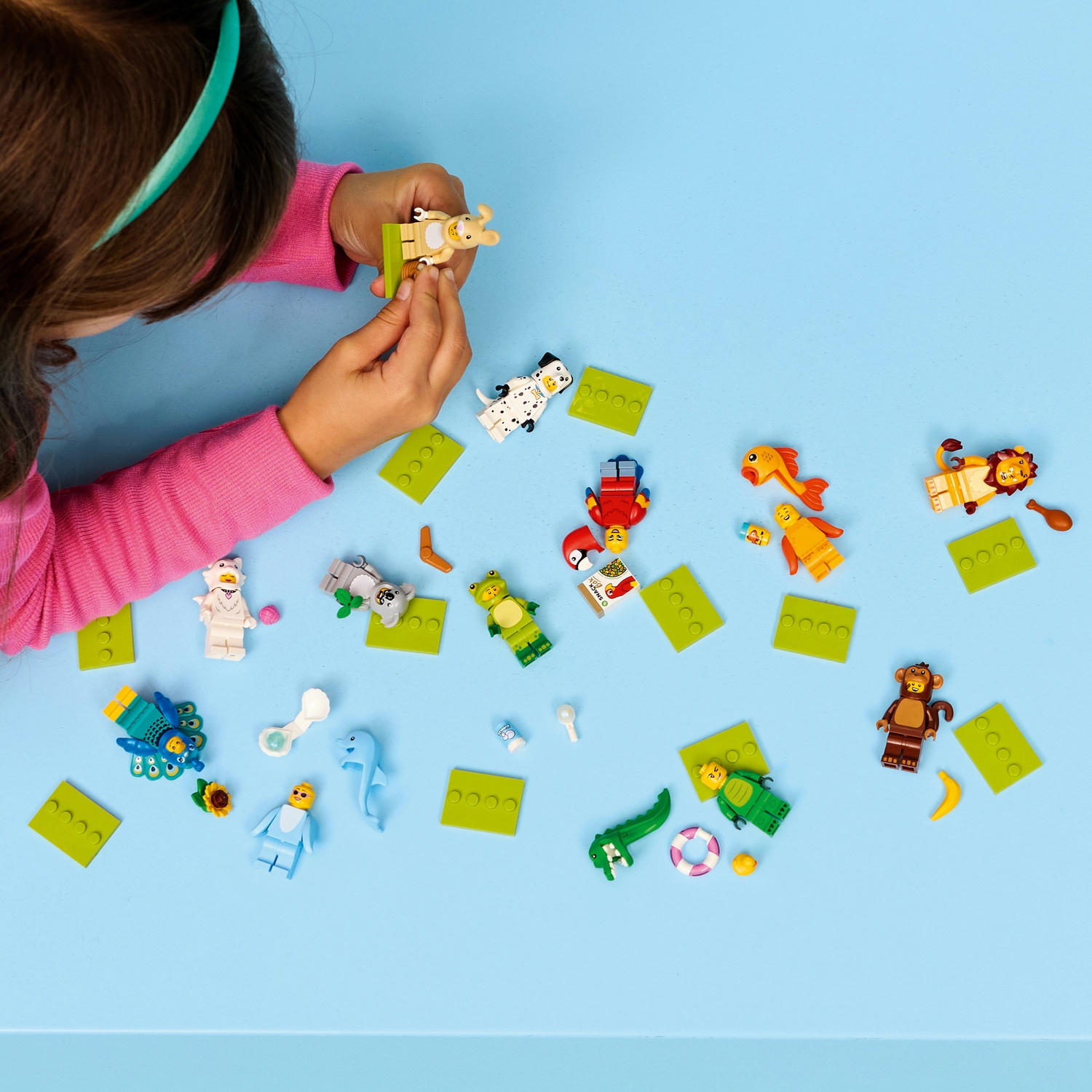 Un bambino gioca con animaletti Lego su una superficie blu. Ci sono vari animali Lego e blocchi verdi sparsi.