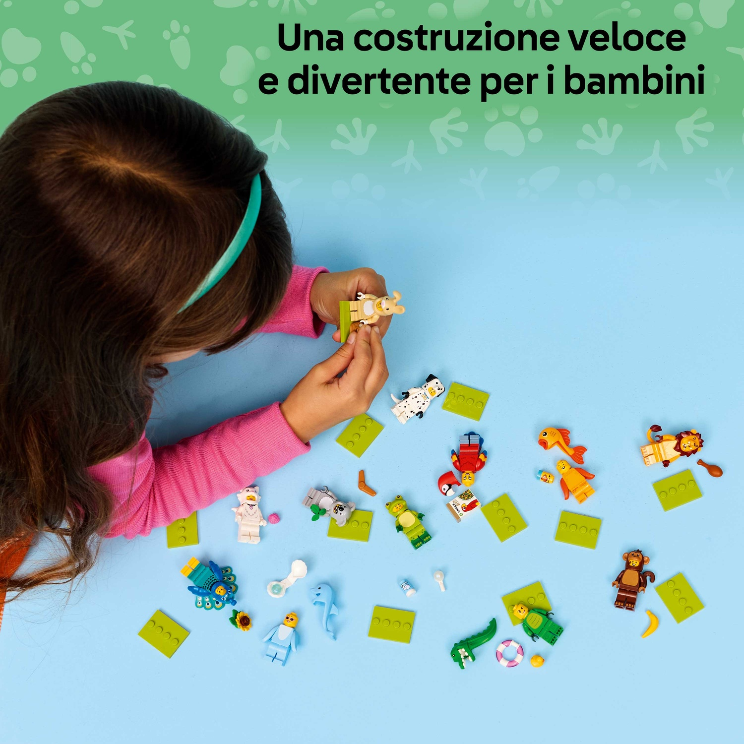 Un bambino gioca con personaggi Lego e basi verdi. Varie figure di animali sono sparse su una superficie blu.