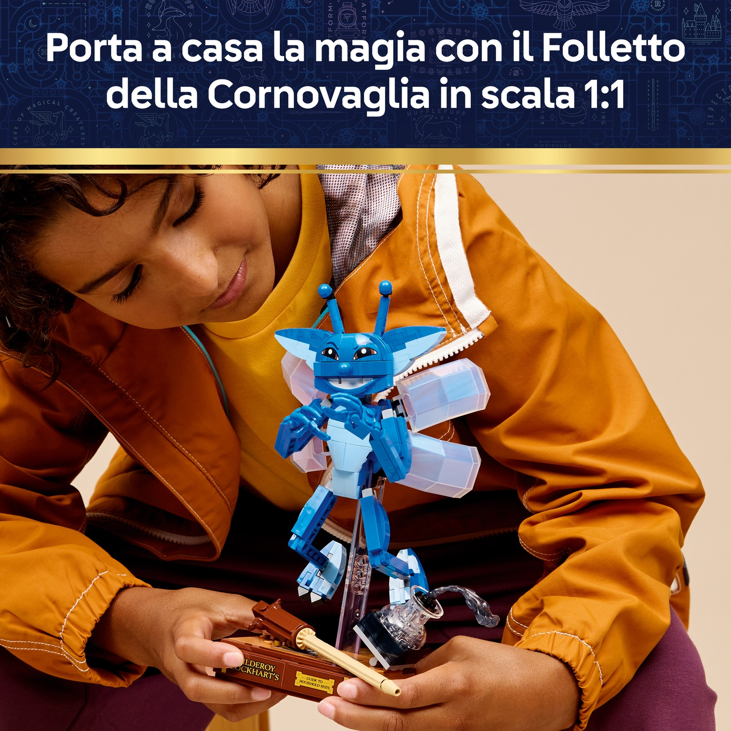 Un bambino tiene in mano un Lego Cornish Pixie blu. Il Pixie è su un supporto. Il bambino indossa una giacca arancione.