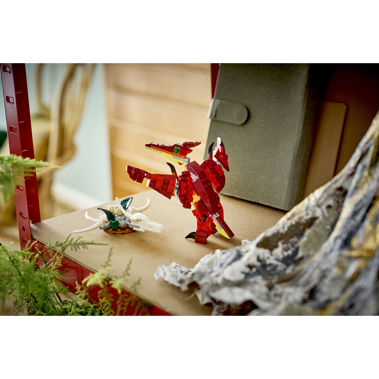 Drago Lego rosso e creatura Lego bianca su scaffale. Felce verde, scaffale marrone e libro verde oliva sullo sfondo.