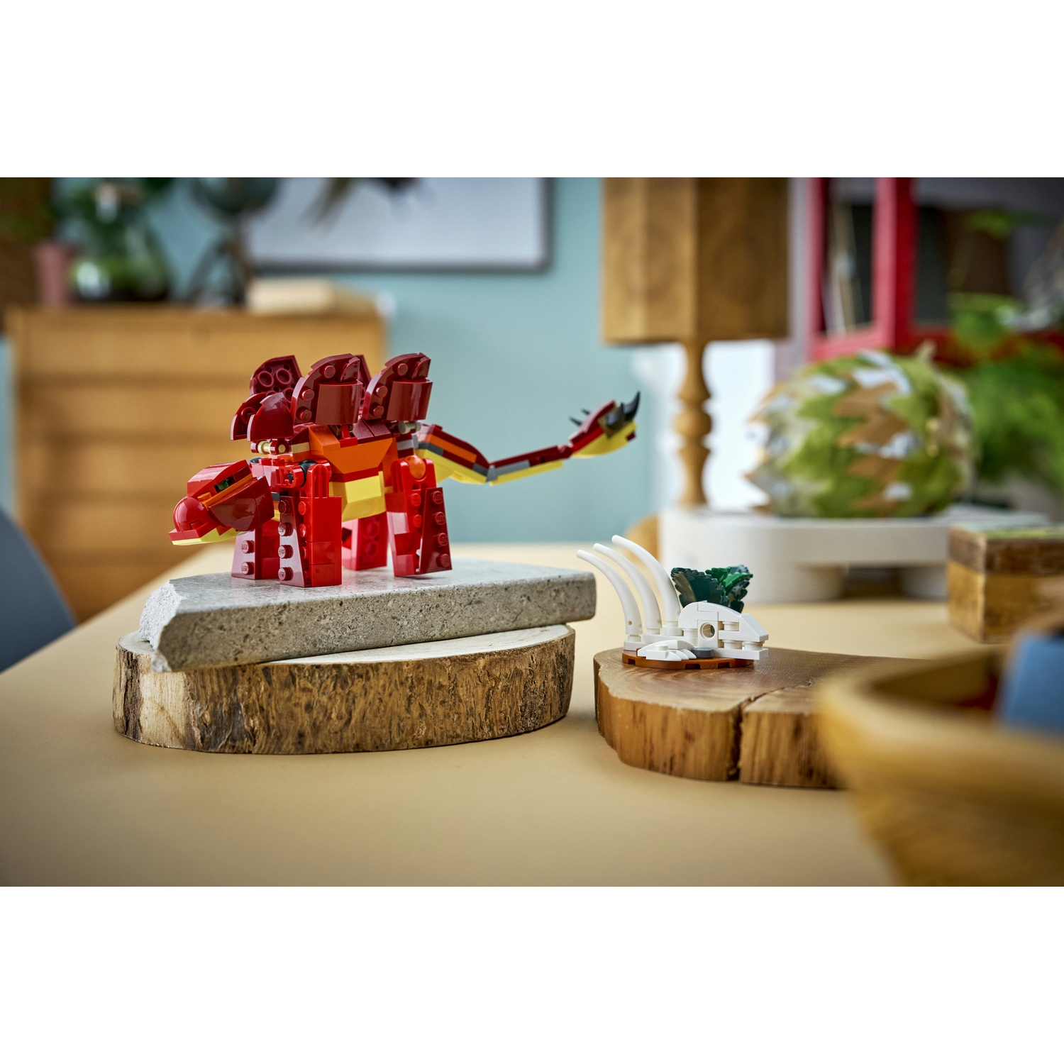 Un dinosauro Lego rosso è su una pietra grigia, un'altra struttura Lego con ossa bianche e foglie verdi è su legno.