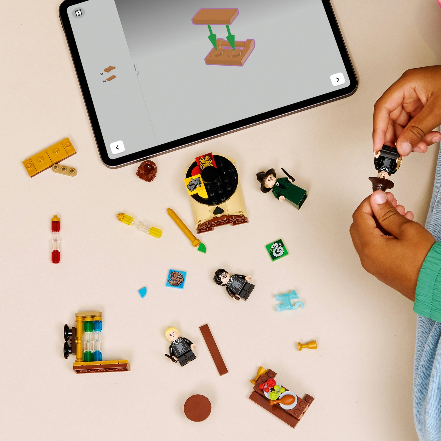 Mani di un bambino che tengono personaggi Lego. Vari pezzi e personaggi Lego sono sparsi attorno a un tablet che mostra le istruzioni.