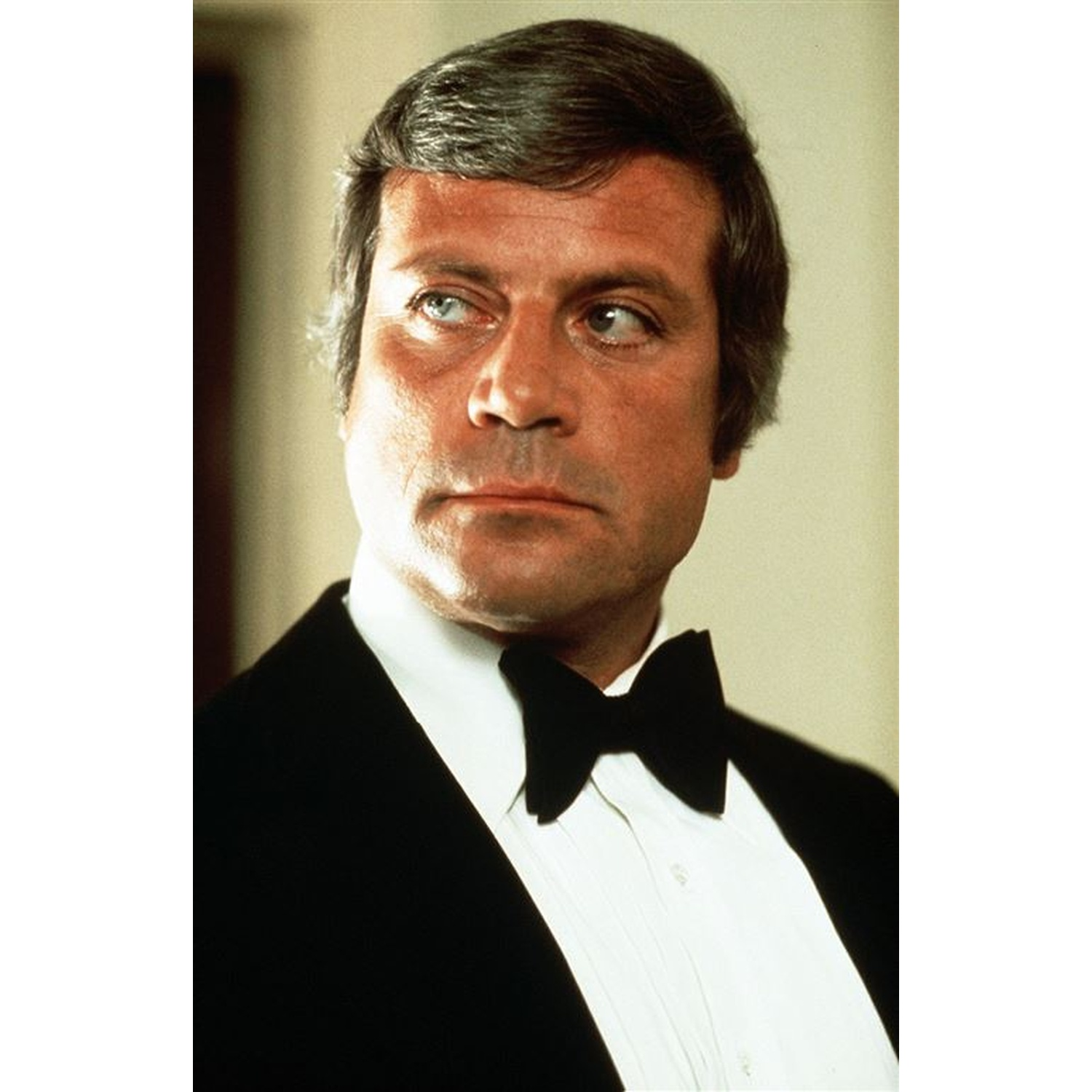 Un homme en smoking, chemise blanche et nœud papillon noir, regardant sur le côté. Il a des cheveux courts et grisonnants et une expression sérieuse.