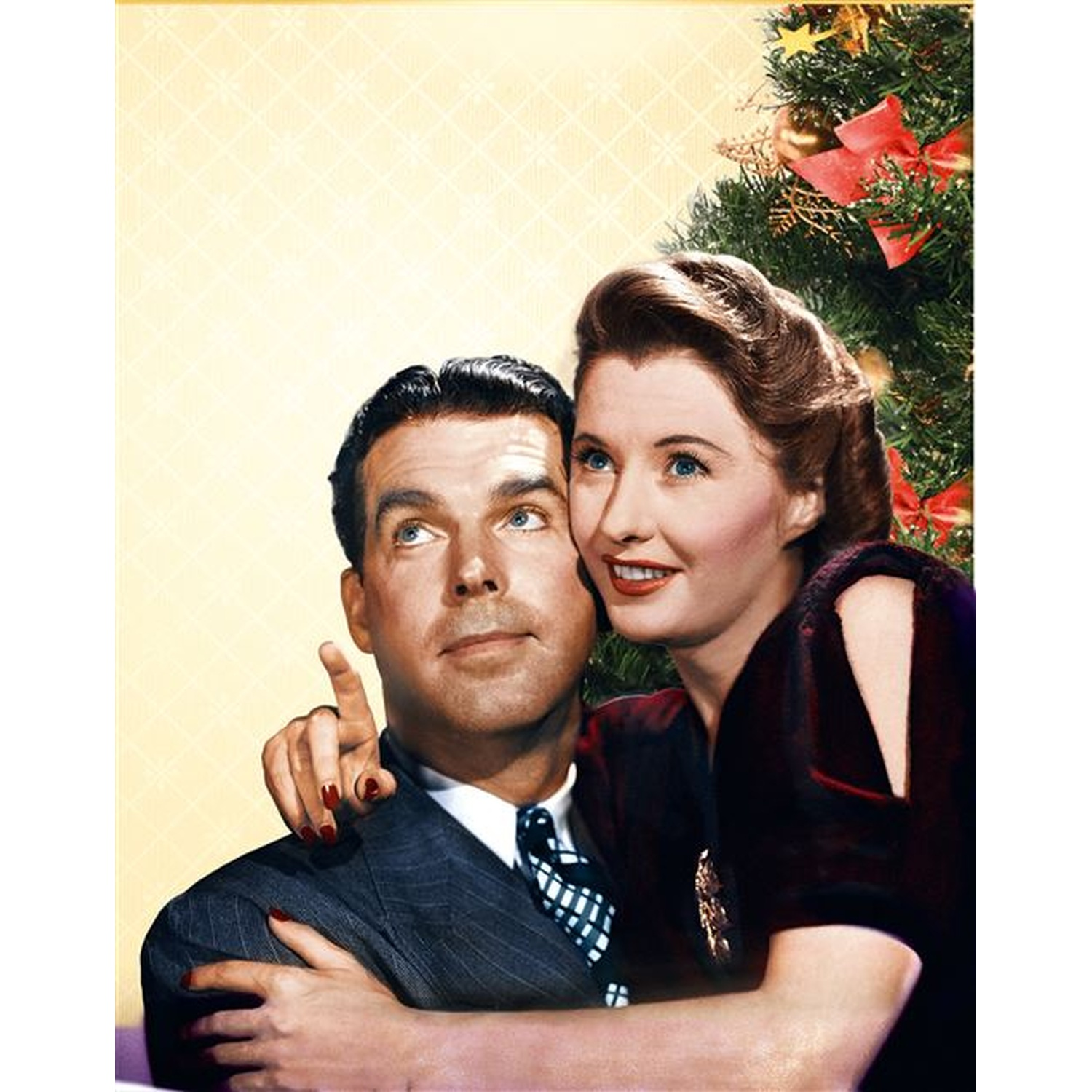 Een man in een pak wijst omhoog, omhelsd door een vrouw. Achter hen een versierde kerstboom. Het paar kijkt omhoog.