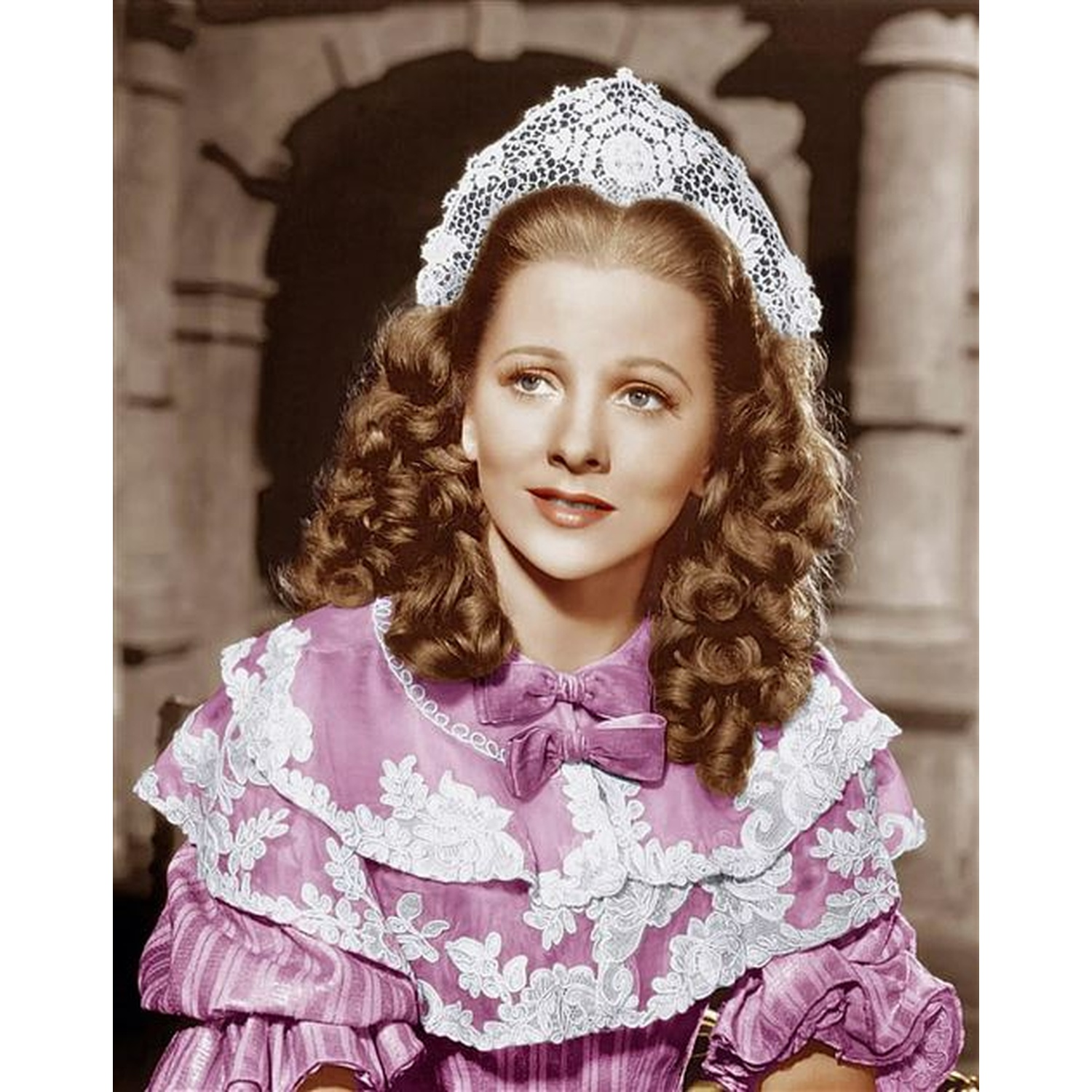 Een vrouw in een roze jurk en een witte kanten hoofdtooi. Ze heeft krullend bruin haar en kijkt opzij.