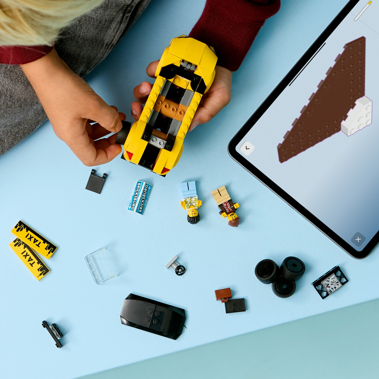 Un bambino assembla un'auto giocattolo gialla, circondato da pezzi Lego, mini figure e un tablet con le istruzioni.