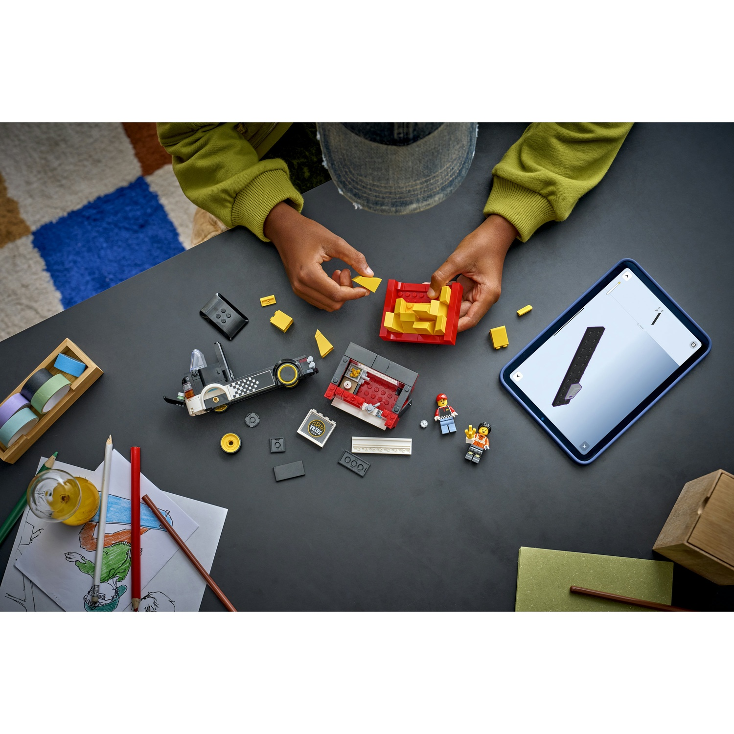 Un bambino assembla mattoncini Lego su un tavolo. Sono visibili parti del set Lego e un tablet con le istruzioni.