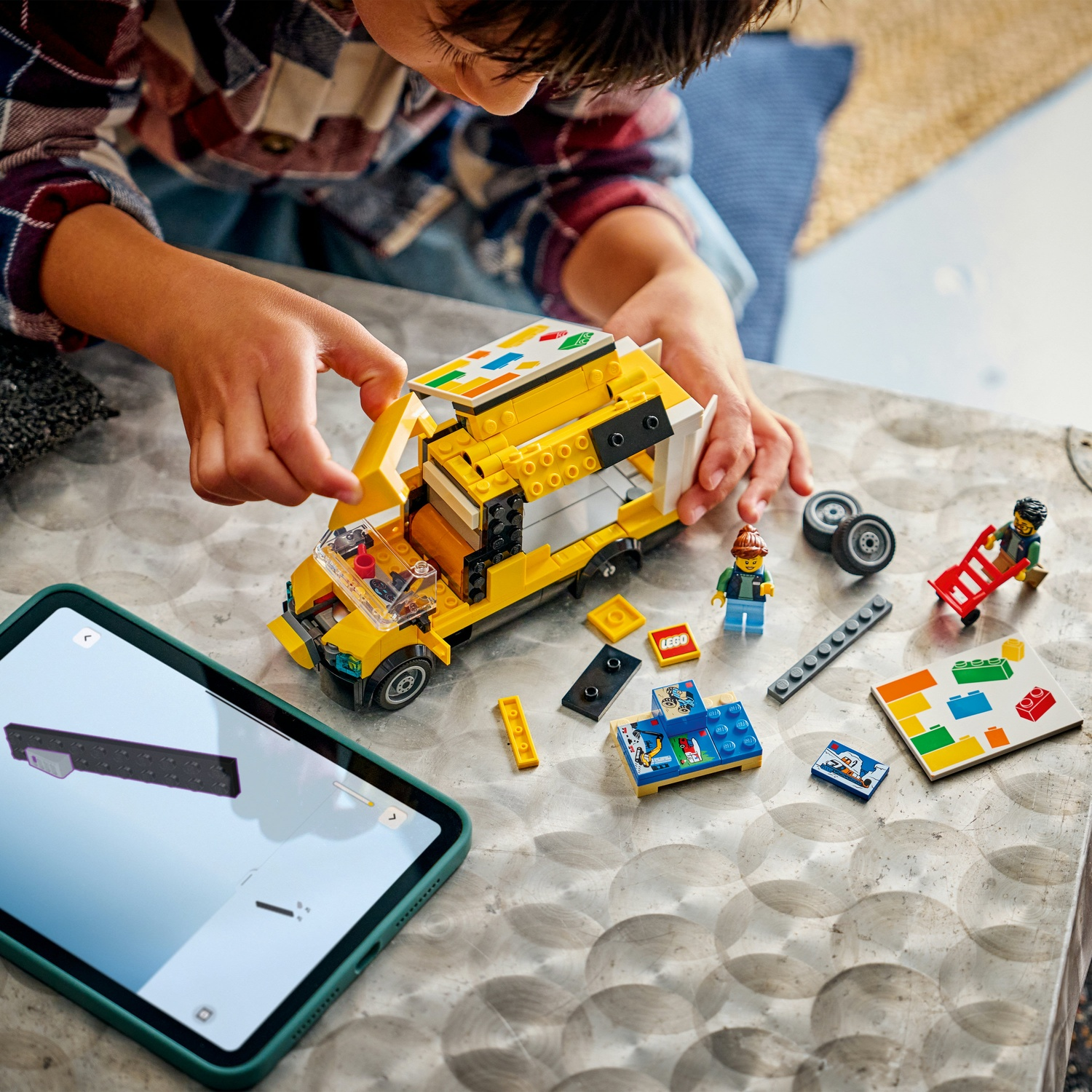 Un bambino sta costruendo un furgone Lego. Il furgone è giallo. C'è un tablet che mostra le istruzioni. Pezzi e figure Lego sono sul tavolo.