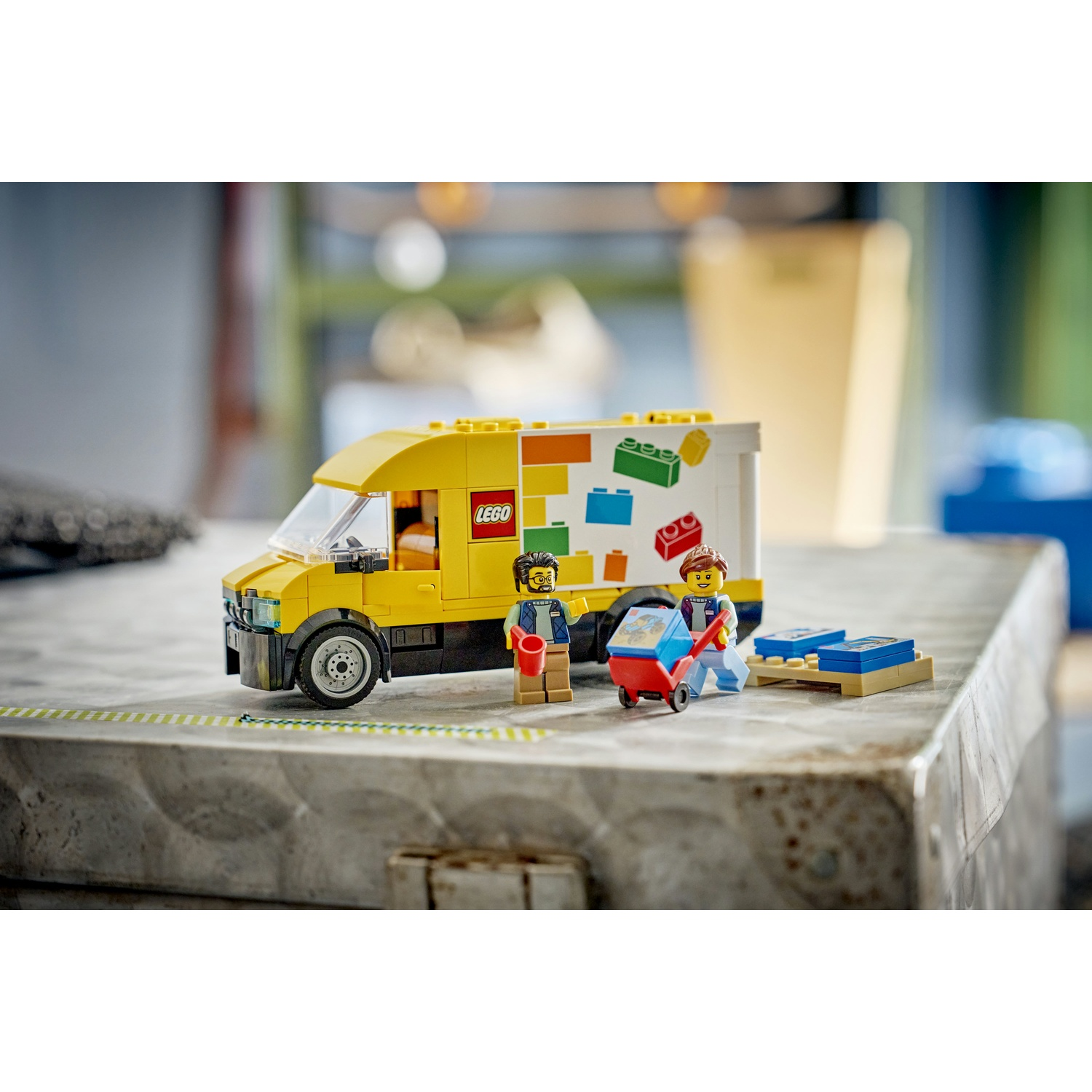 Un set Lego con un furgone giallo, personaggi Lego e un carrello. Il camion ha il logo Lego e blocchi colorati.