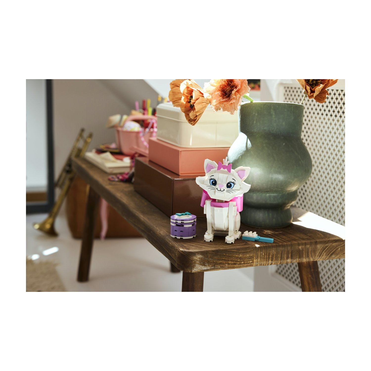 Un gatto Marie Lego è seduto su una panchina di legno. Fiori in un vaso sono dietro il gatto. Altri oggetti sono sulla panchina.
