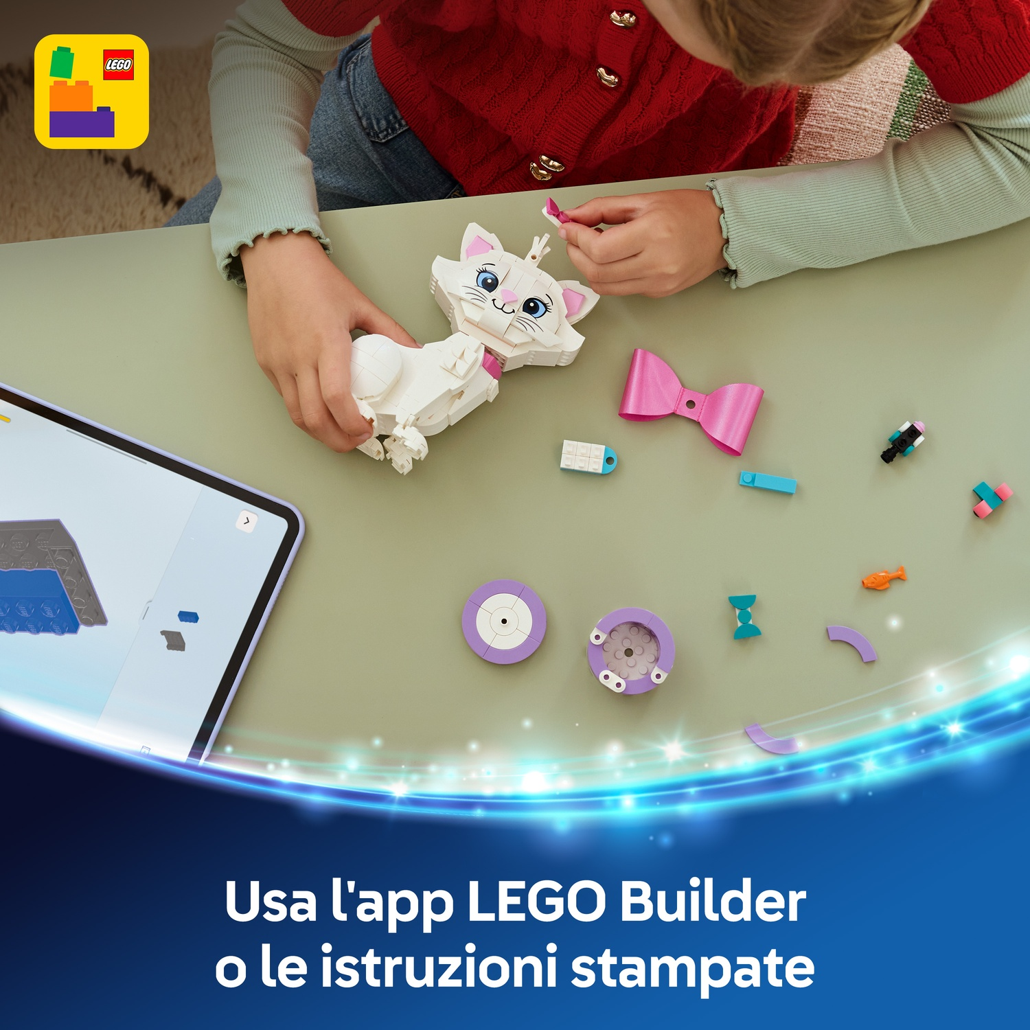 Un bambino assembla un gatto LEGO bianco. Vari pezzi LEGO e un tablet sono su una superficie verde.