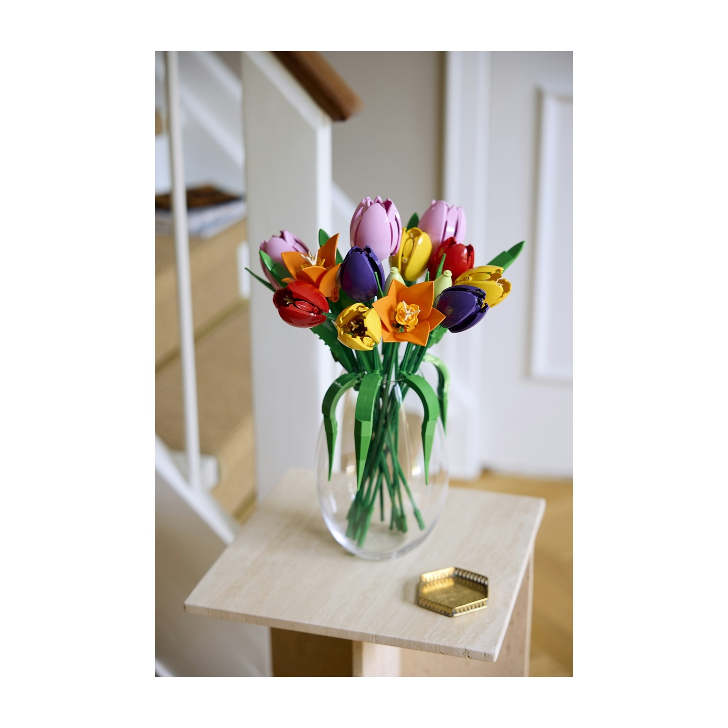Un vaso di tulipani colorati su un tavolo di legno. Sullo sfondo una scala e una porta.