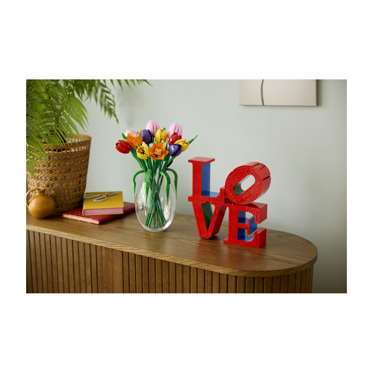 Un mobile in legno con un vaso di fiori colorati, una scultura 'LOVE' e una felce in un cesto sopra.