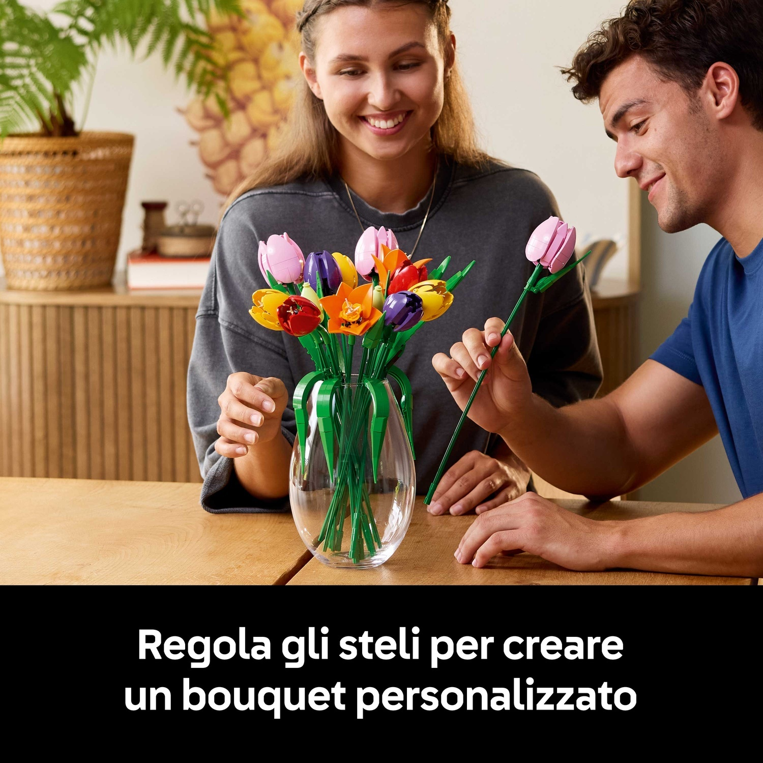 Una coppia che sistema un bouquet di tulipani Lego in un vaso. I fiori sono di vari colori. Sorridono e guardano i fiori.