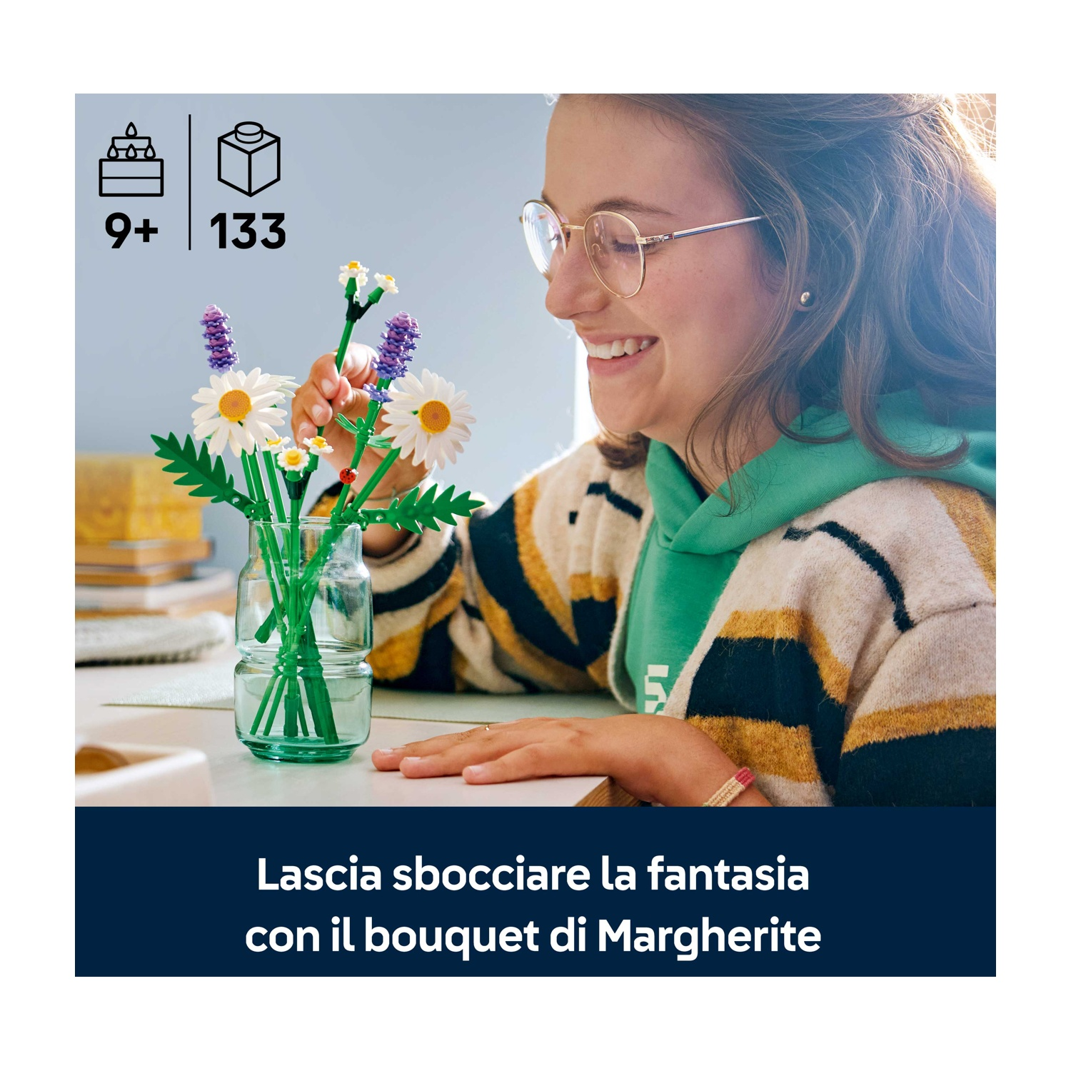 Una donna sorride, sistemando un bouquet di fiori Lego in un vaso di vetro. Il set comprende margherite, lavanda e steli verdi.