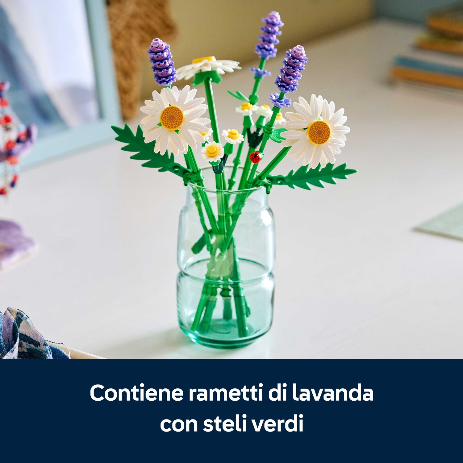 Un vaso di vetro con fiori Lego: margherite, lavanda e piccoli fiori gialli. Il vaso è su un tavolo bianco.