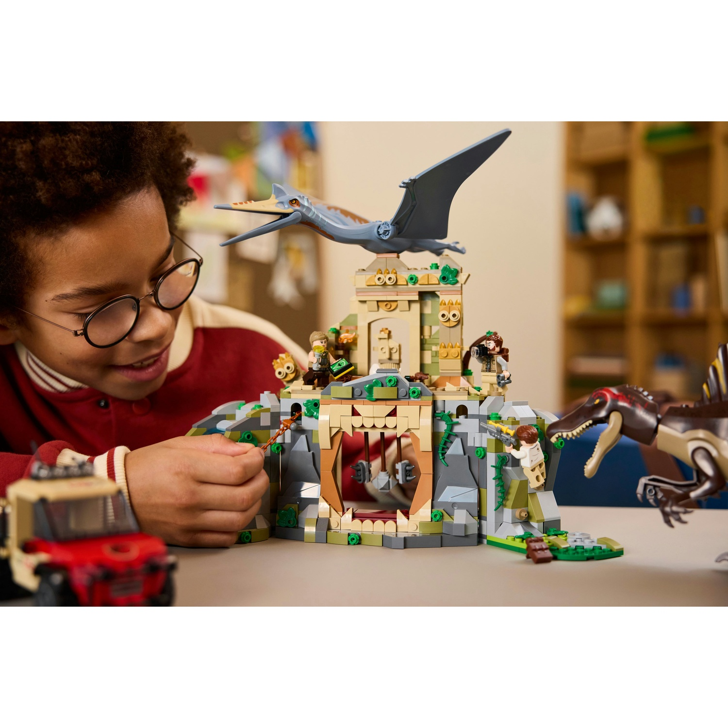 Un bambino gioca con un set Lego, con dinosauri e un edificio. Un Pterodattilo vola sopra l'edificio.