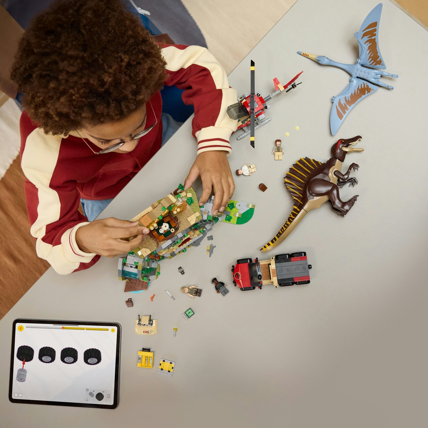 Un bambino sta costruendo un set Lego con dinosauri e un elicottero. Un tablet mostra le istruzioni.