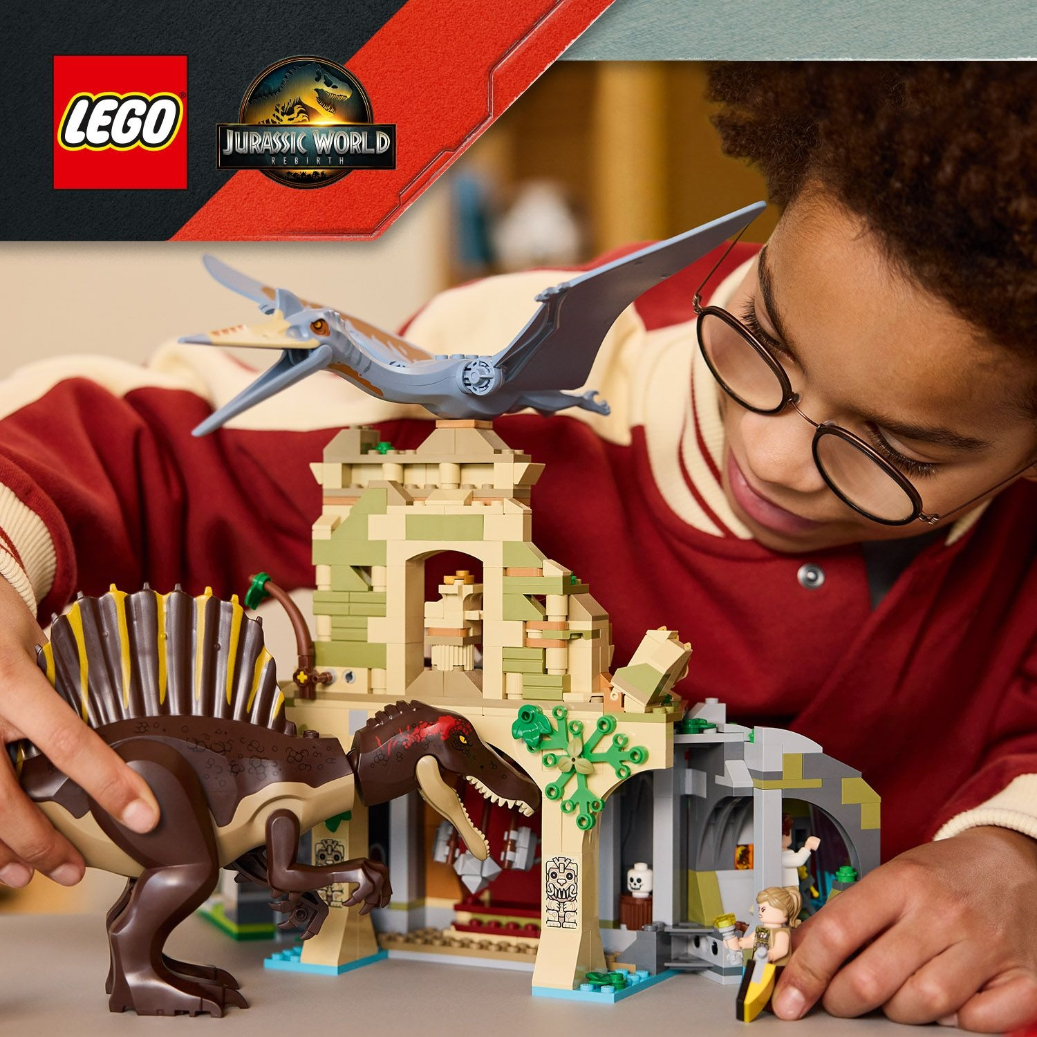 Un bambino con gli occhiali gioca con un set Lego Jurassic World, tra cui dinosauri e una struttura a tempio.