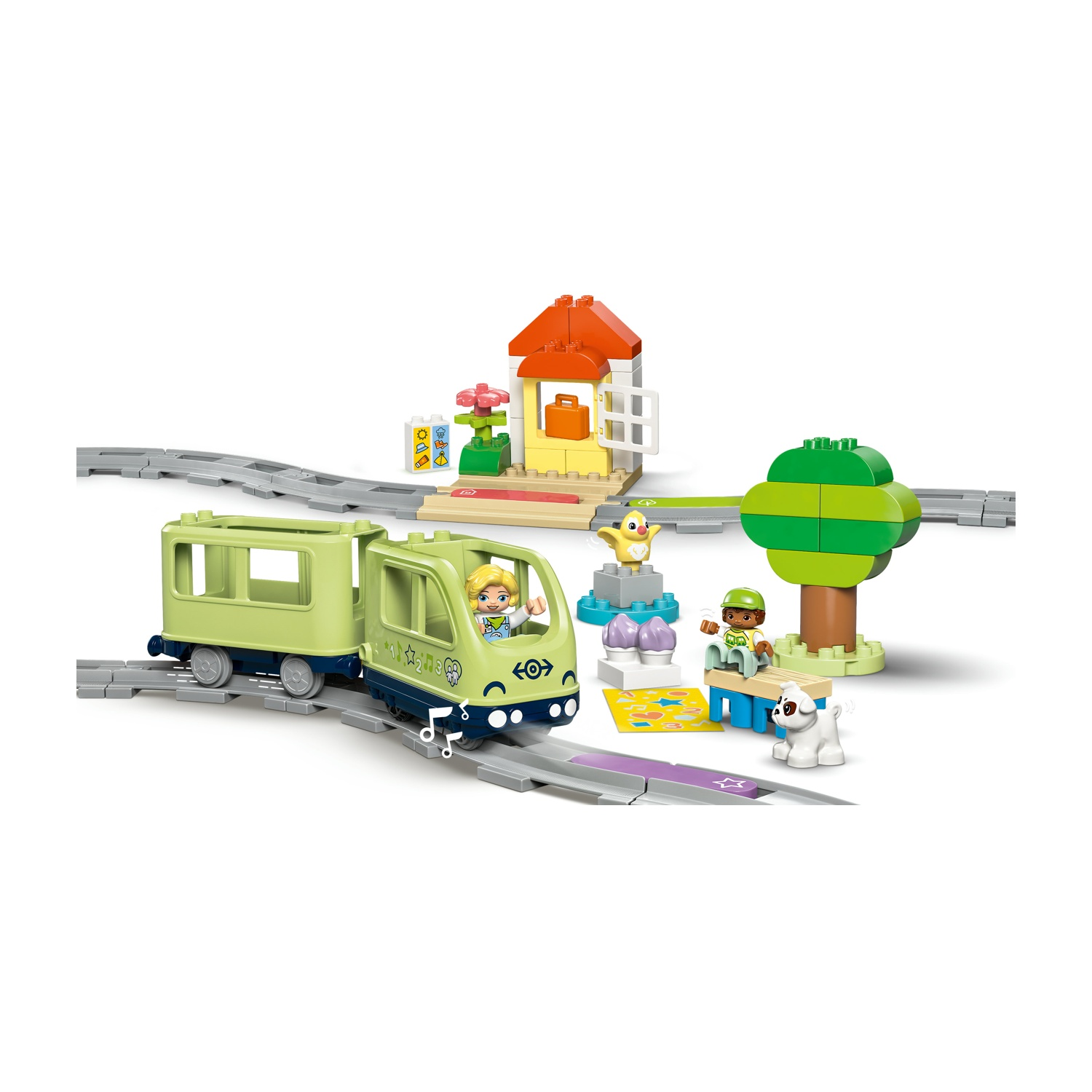 Un set di treni Lego. Include un treno, una stazione con una casa, un albero, una panchina con una persona, un cane e un uccello.