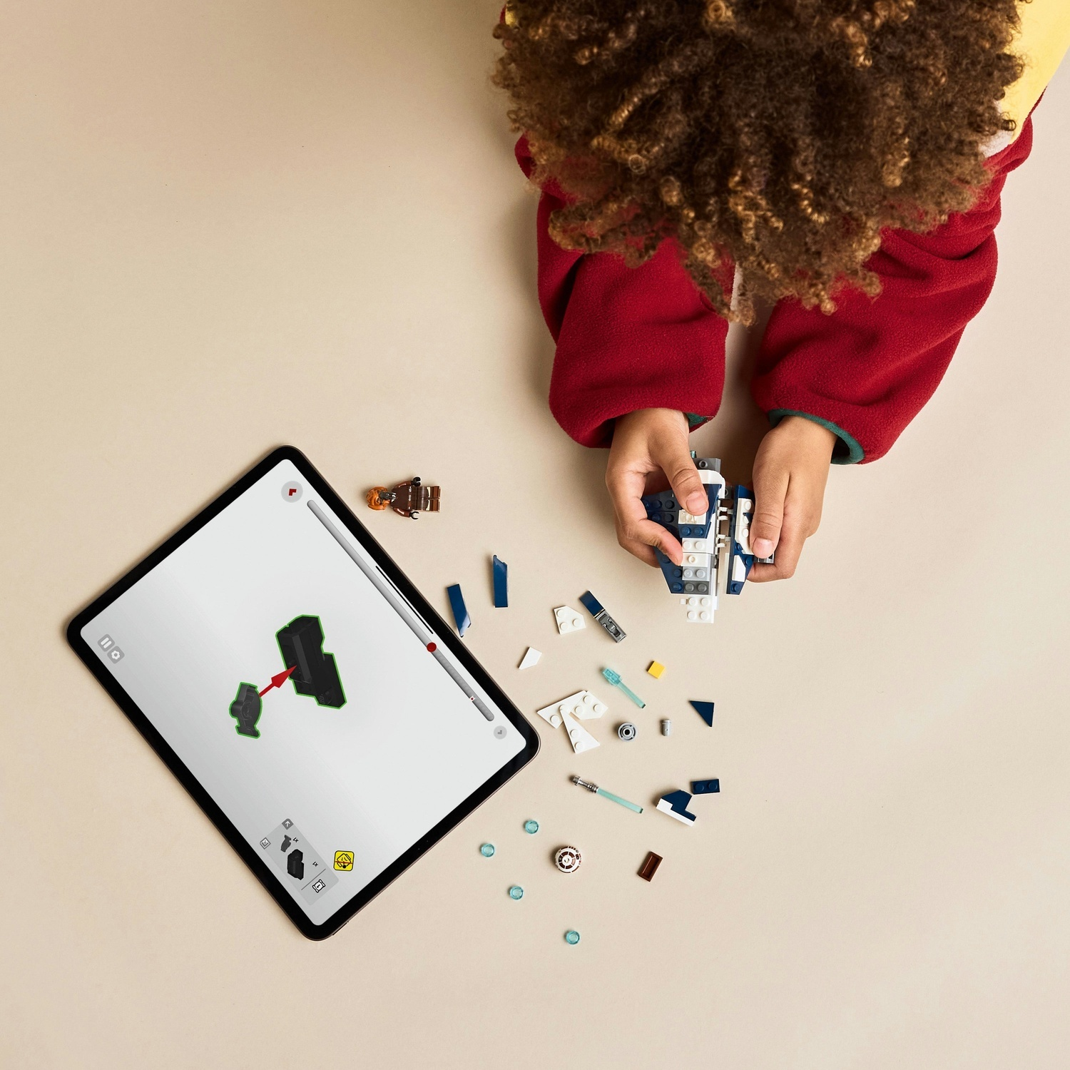 Un bambino costruisce con mattoncini LEGO, seguendo le istruzioni su un tablet. Mattoncini e una piccola figura LEGO sono sparsi sul tavolo.