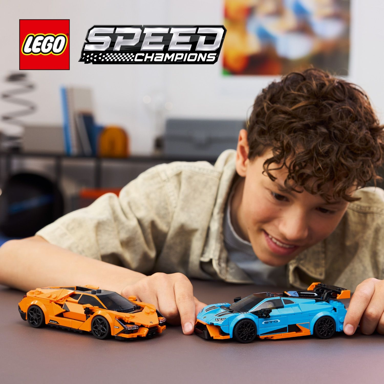 Un ragazzo sorride a due auto Lego Speed Champions, arancione e blu, su un tavolo. Il logo Lego e il logo Speed Champions sono visibili.