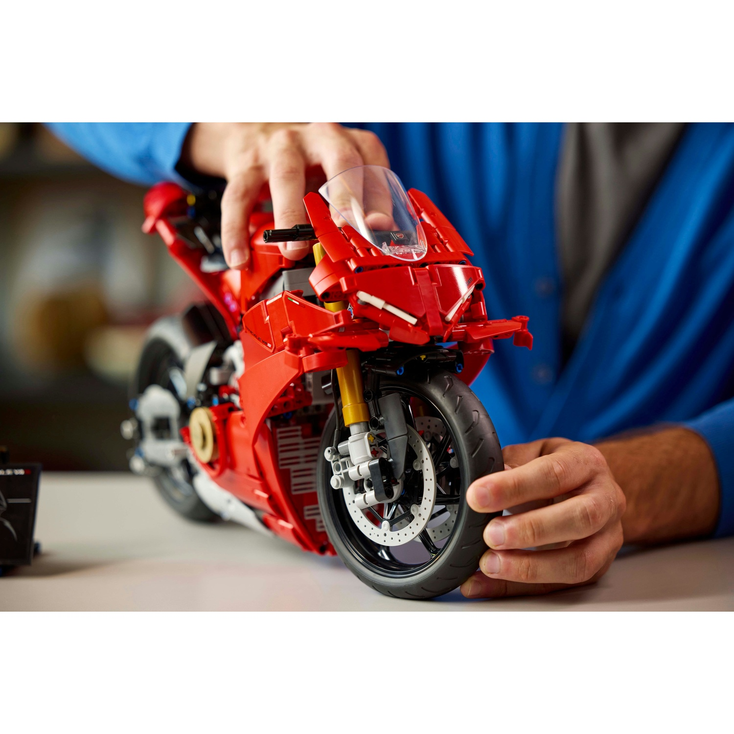 Una persona tiene in mano una moto Lego rossa. La moto è su una superficie bianca. Un maglione blu è sullo sfondo.