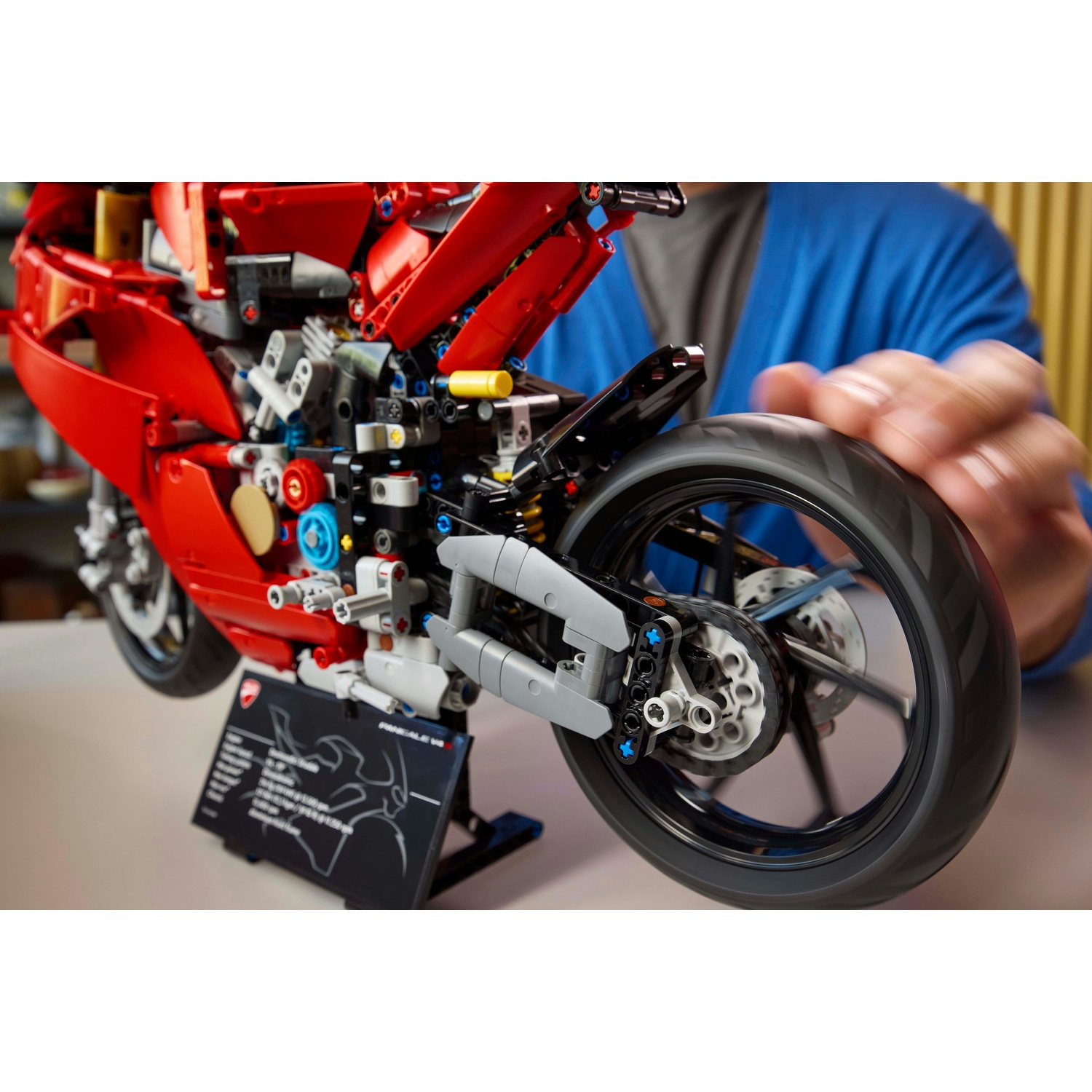 Un modello di moto Lego rosso. Una persona tiene la ruota posteriore, con componenti e un supporto visibili.