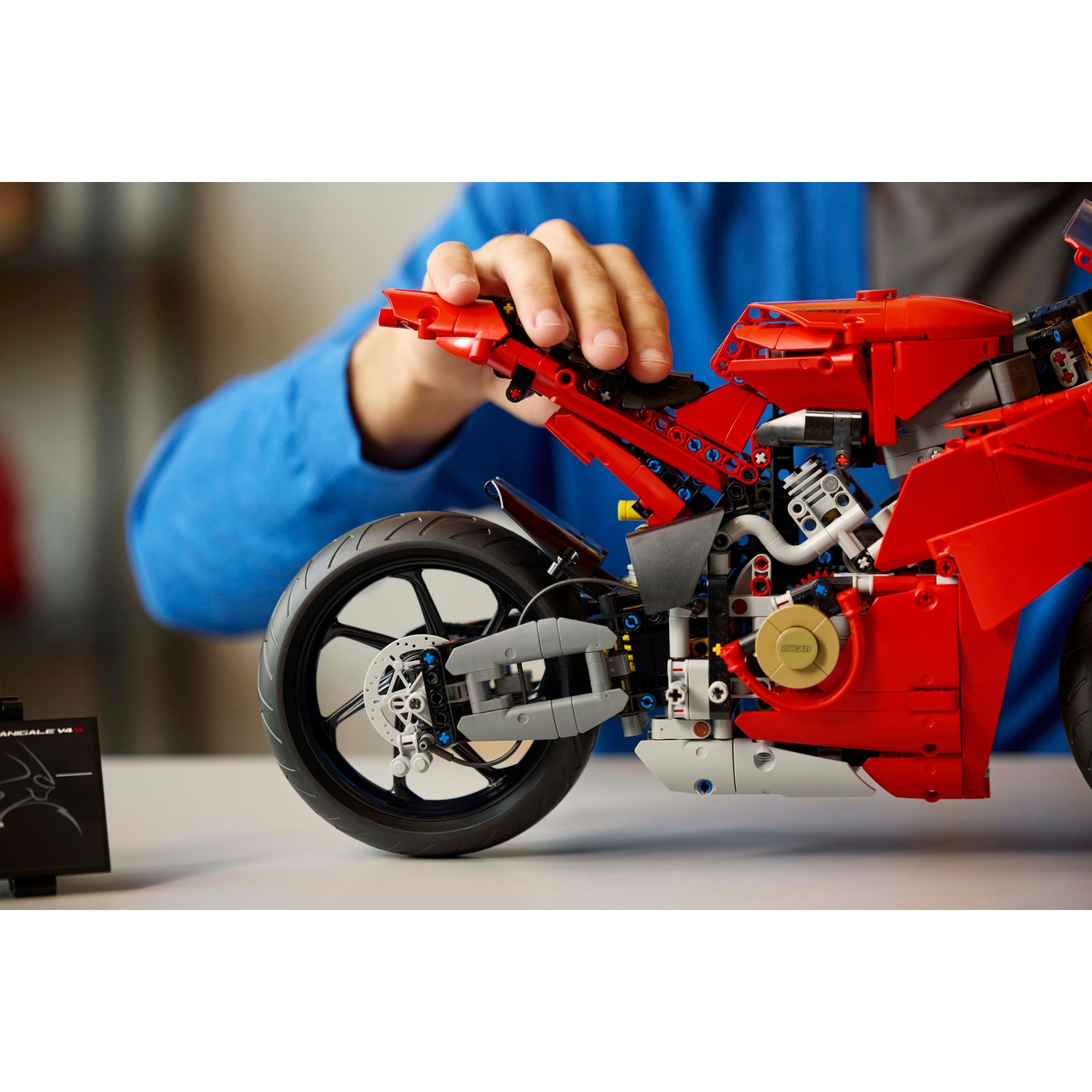 Una persona assembla un modello di moto Ducati rossa. Il modello è su un tavolo. La mano della persona è sul modello.